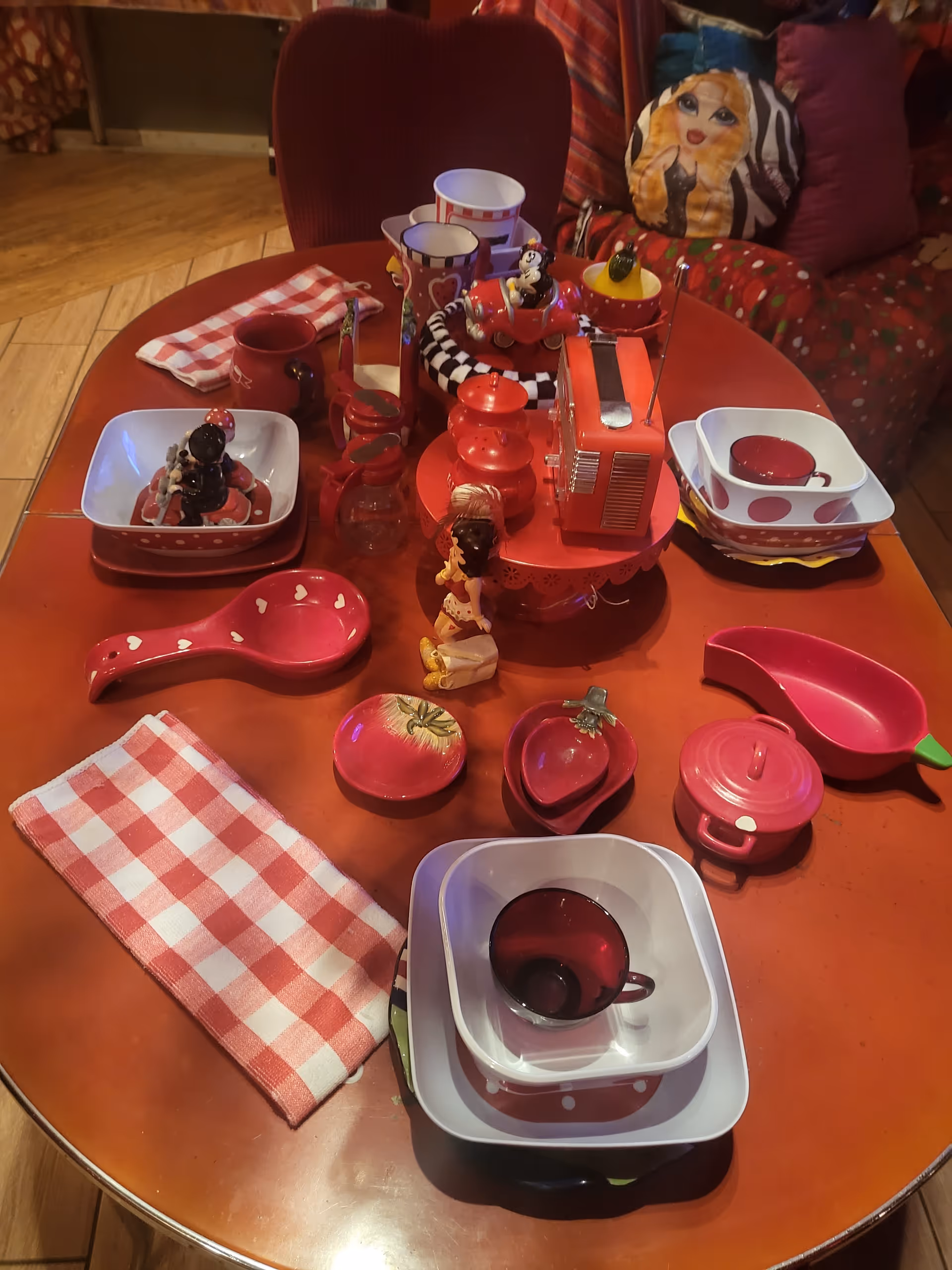 Round wooden table with red toy dishes and kitchen playset in a cozy living space.