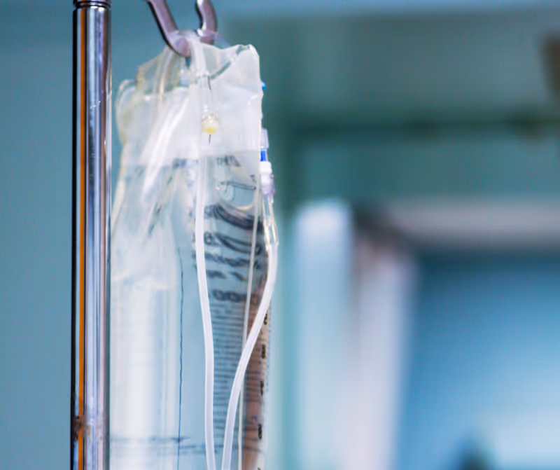 Close view of an IV drip bag and tubing in a medical setup.