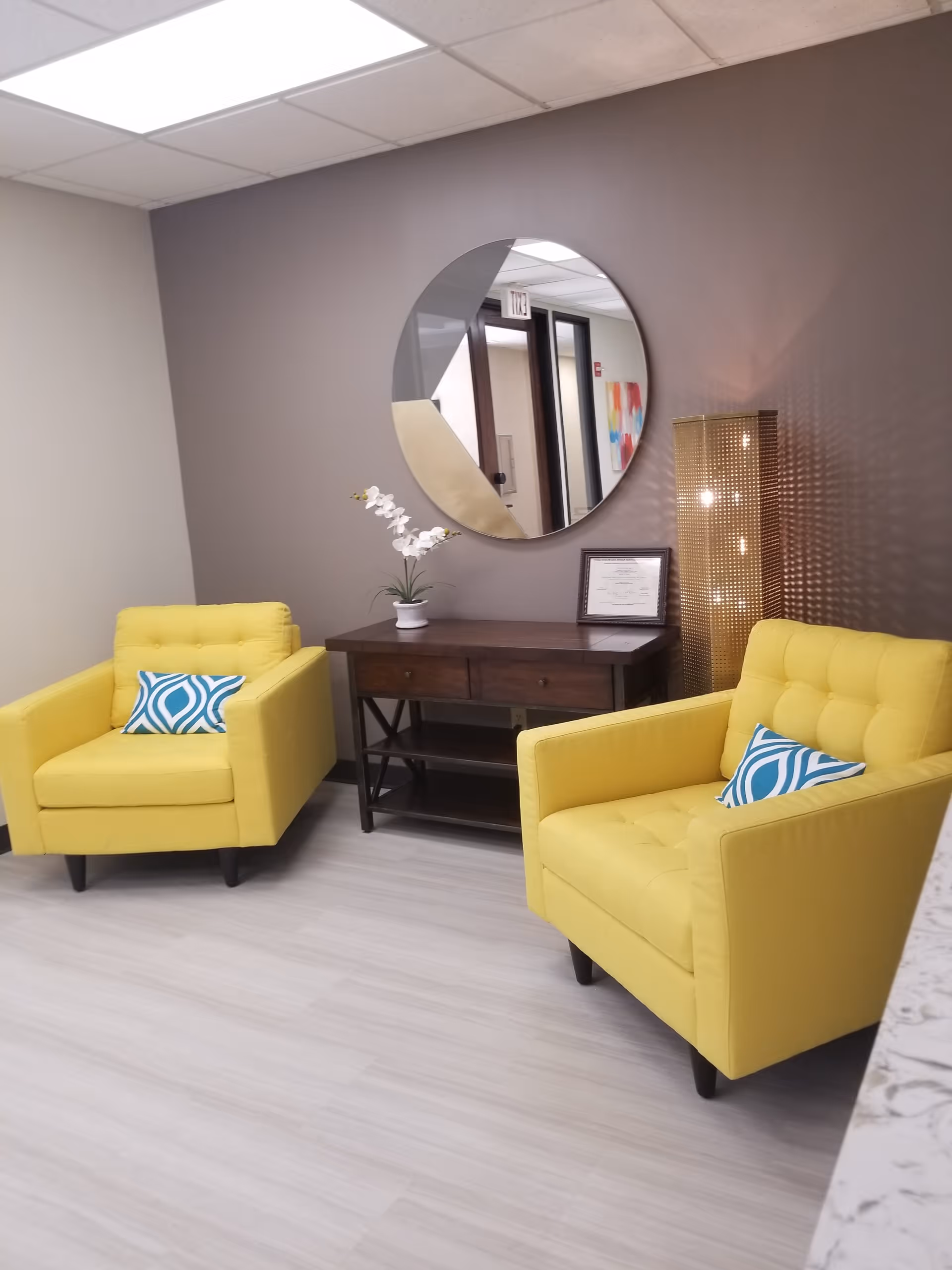 Bright lobby seating area with two yellow chairs, round mirror, and console table.