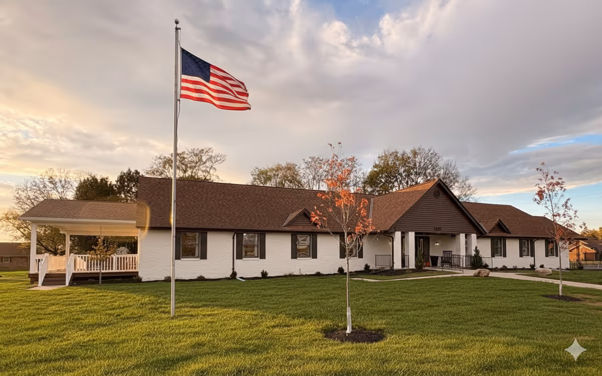 Front exterior of a single-story senior living facility with flag and green lawn.