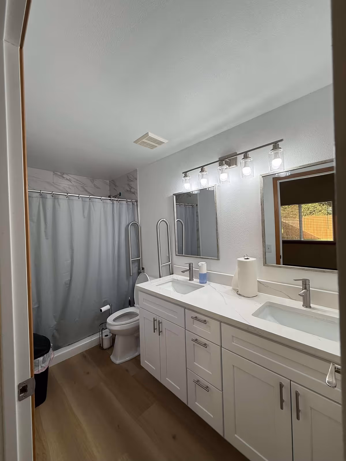 Bright bathroom with double vanity, mirrors, shower curtain, and accessible grab bars.