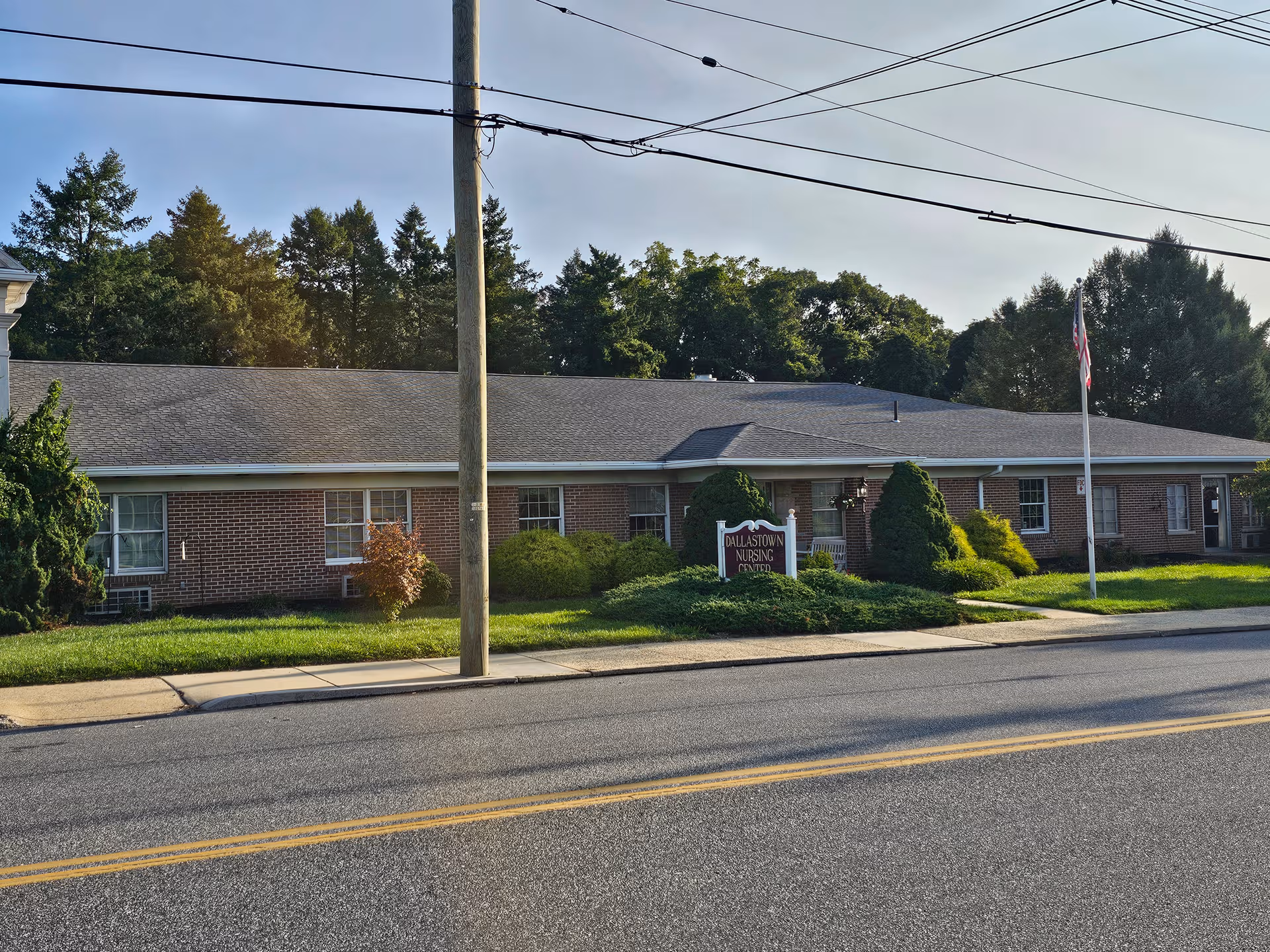 A brick, single-story senior living building with manicured lawn, sign, and flagpole.