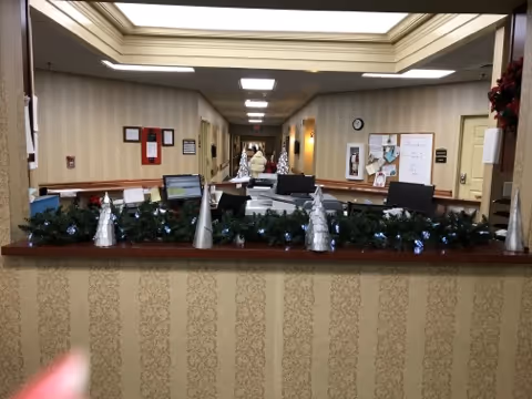 Reception desk area decorated with garlands and silver cone-shaped ornaments, with a hallway extending behind it featuring beige patterned wallpaper, bulletin boards, and ceiling lights.