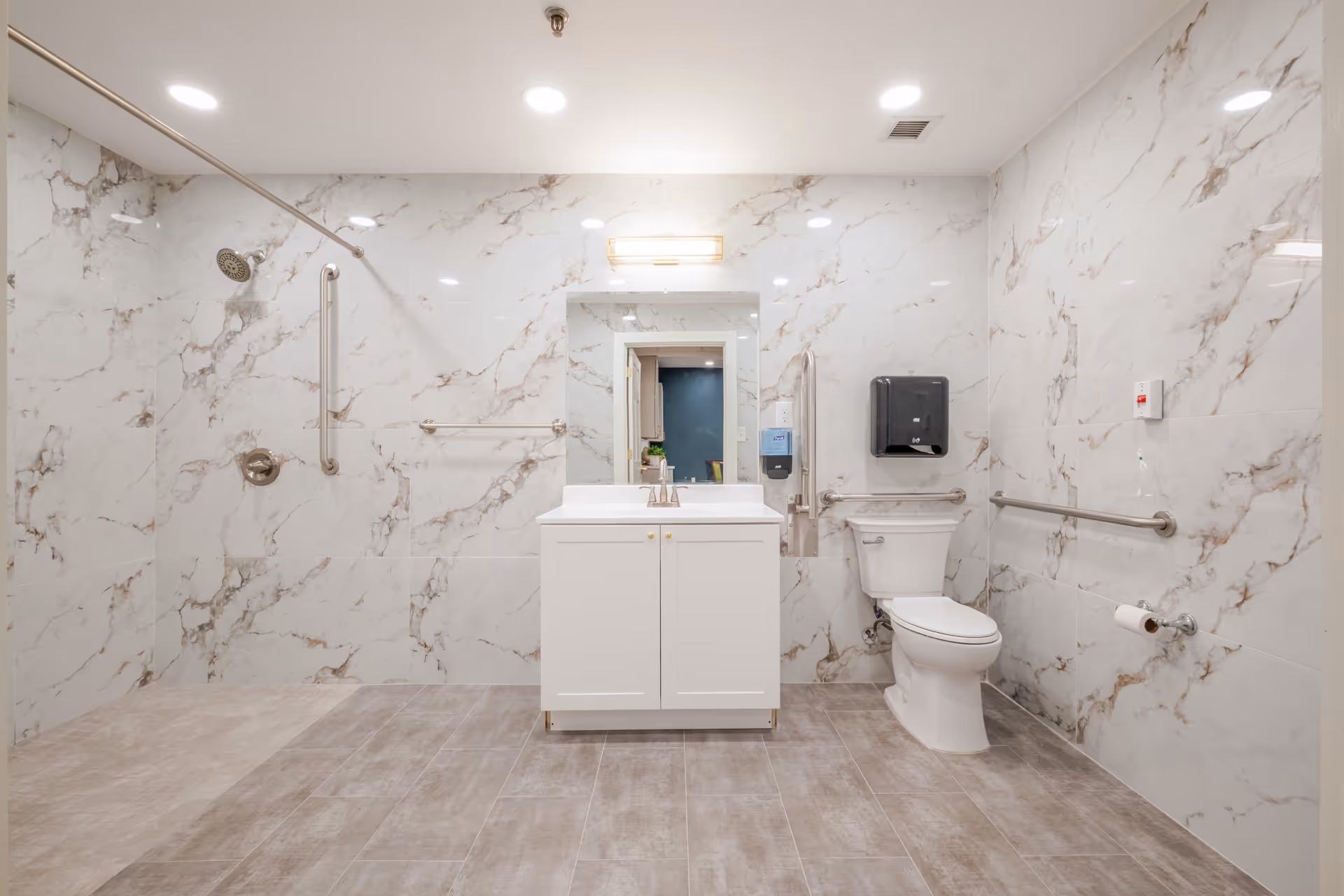 Accessible bathroom with marble walls, walk-in shower, vanity, mirror, toilet, and grab bars.