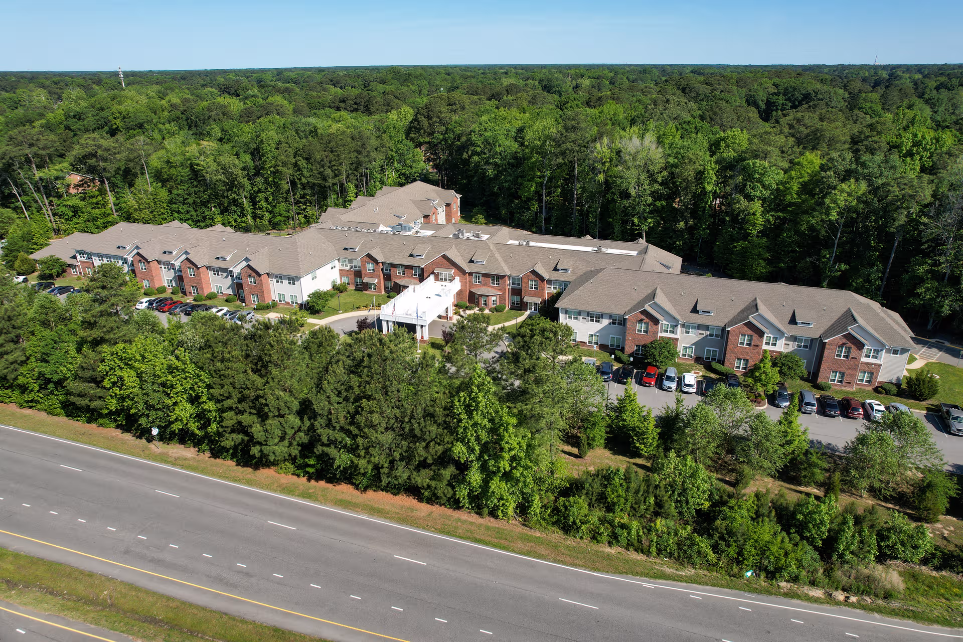 Aerial exterior view of Harmony on the Peninsula senior living campus amid trees and a roadway