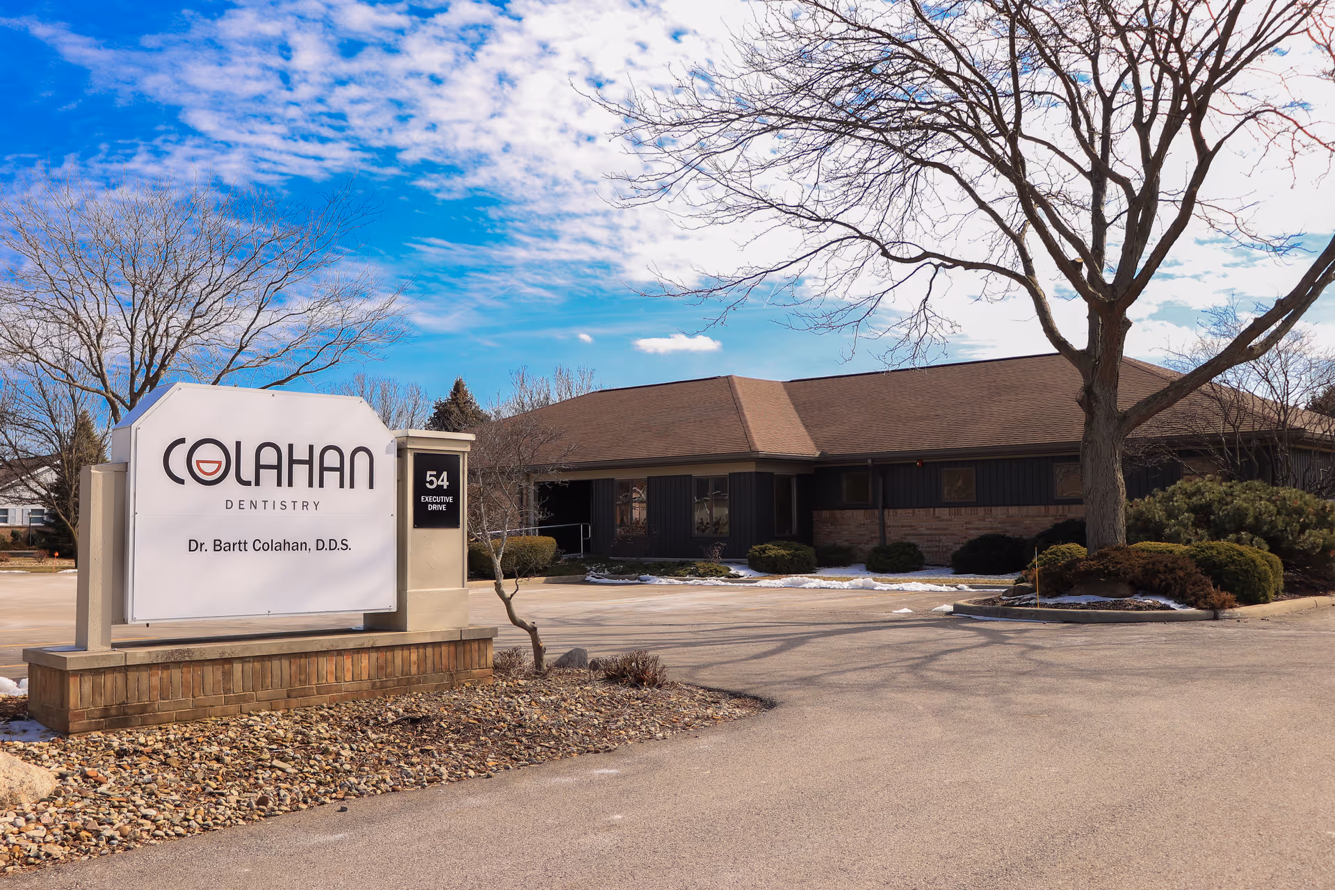 Exterior view of a single-story building with a Colahan Dentistry sign and landscaped parking.