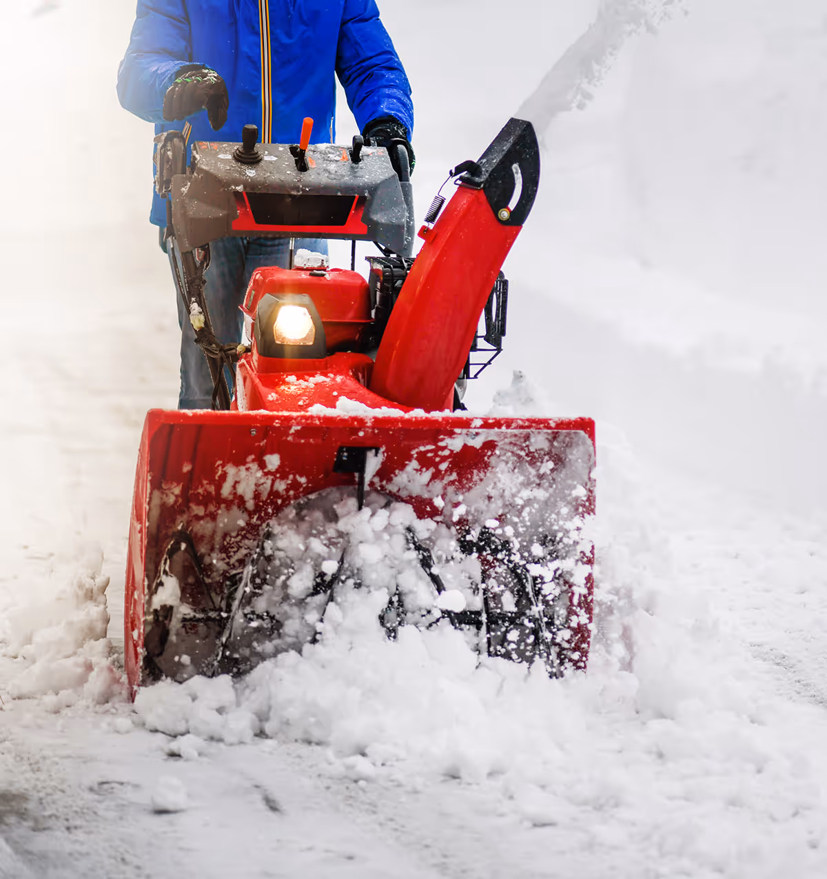 Person operating a red snow blower clearing snow from a pathway outdoors.