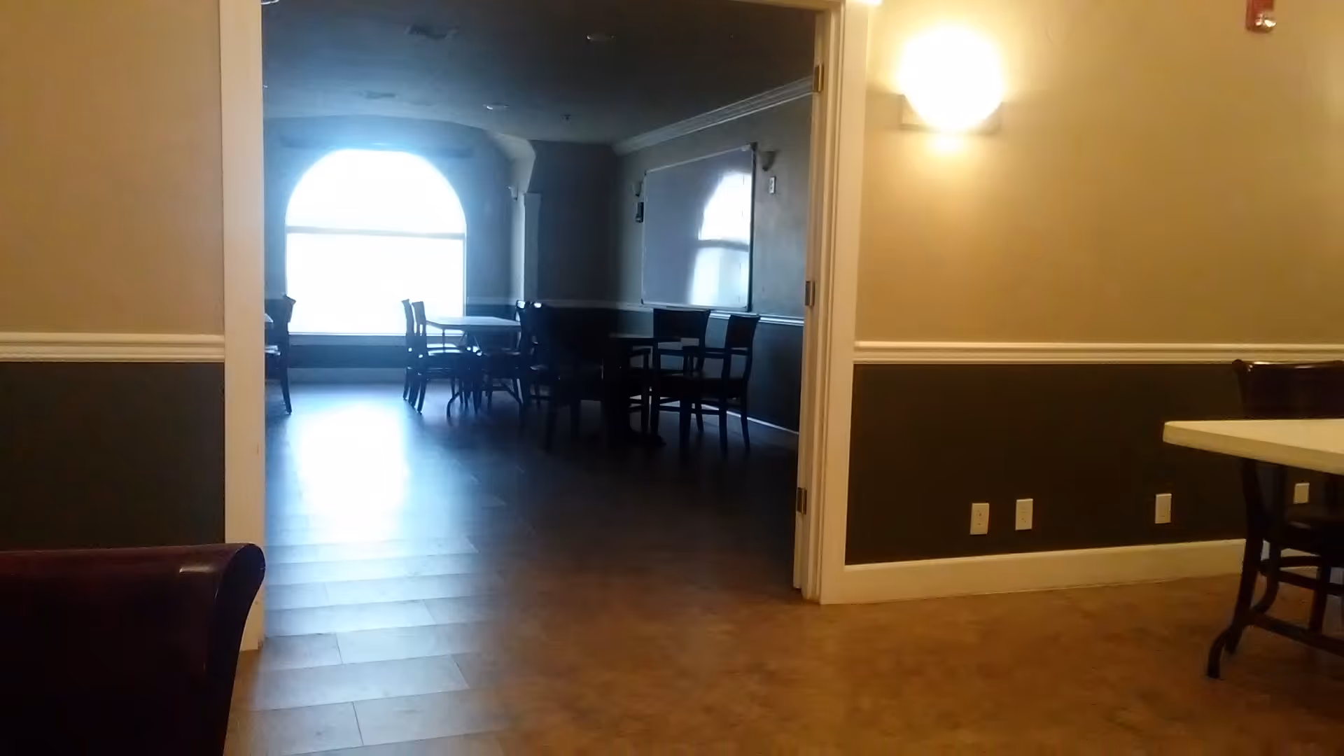 Interior of a senior living facility showing a dining area with arched window and tables.