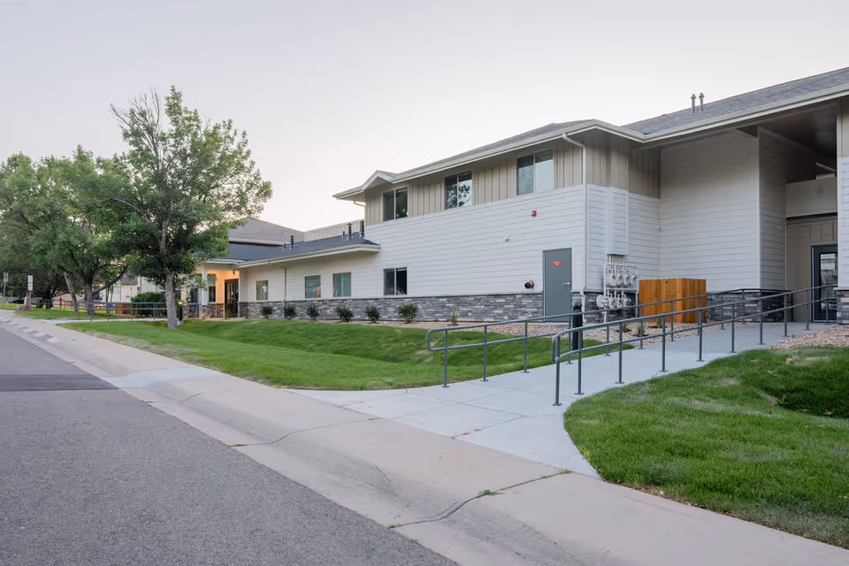 Modern senior living facility exterior with ramp, walkway, lawn, and trees