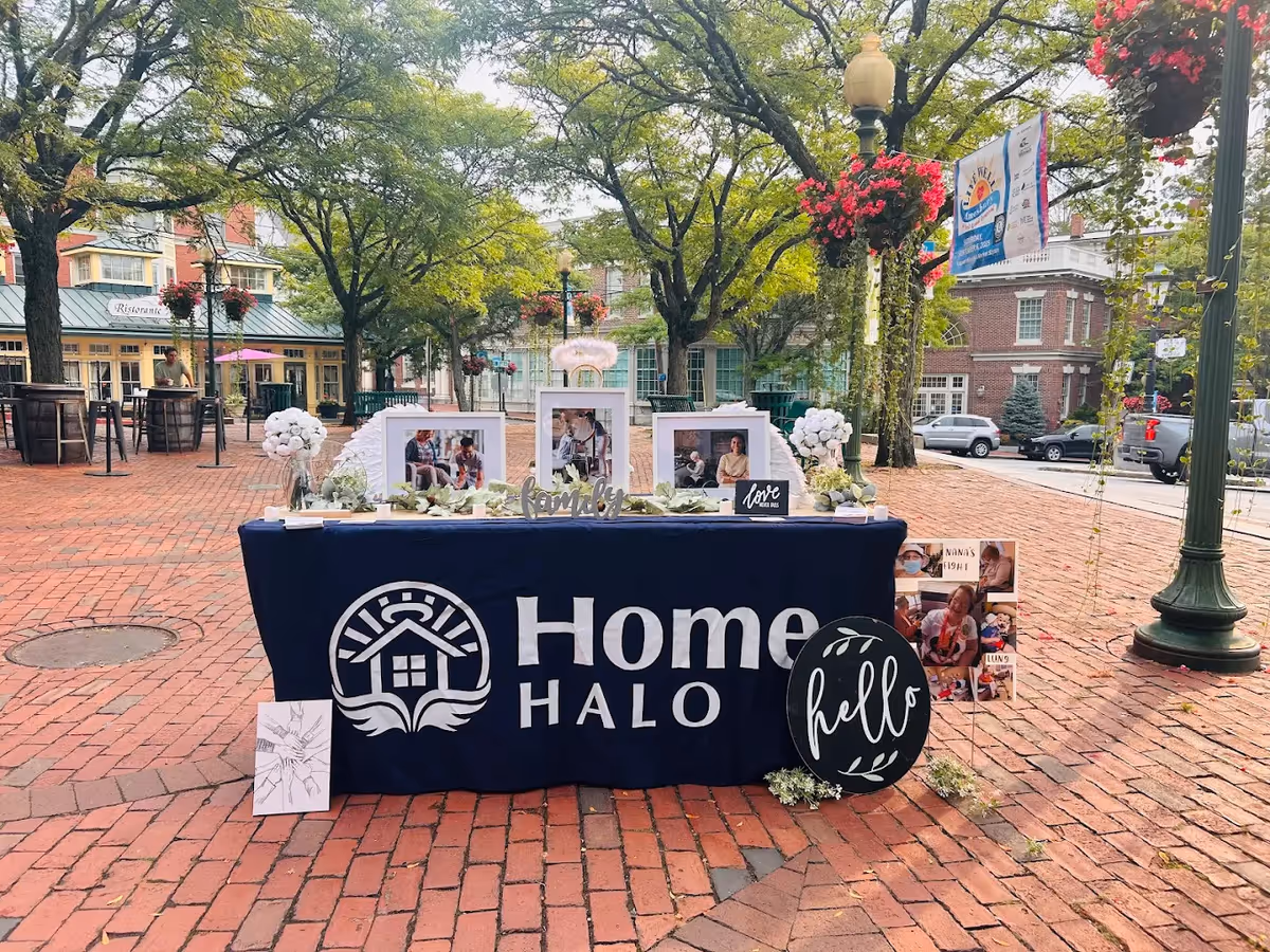 Outdoor promotional table for Home Halo Plano with photos, flowers, and signage.