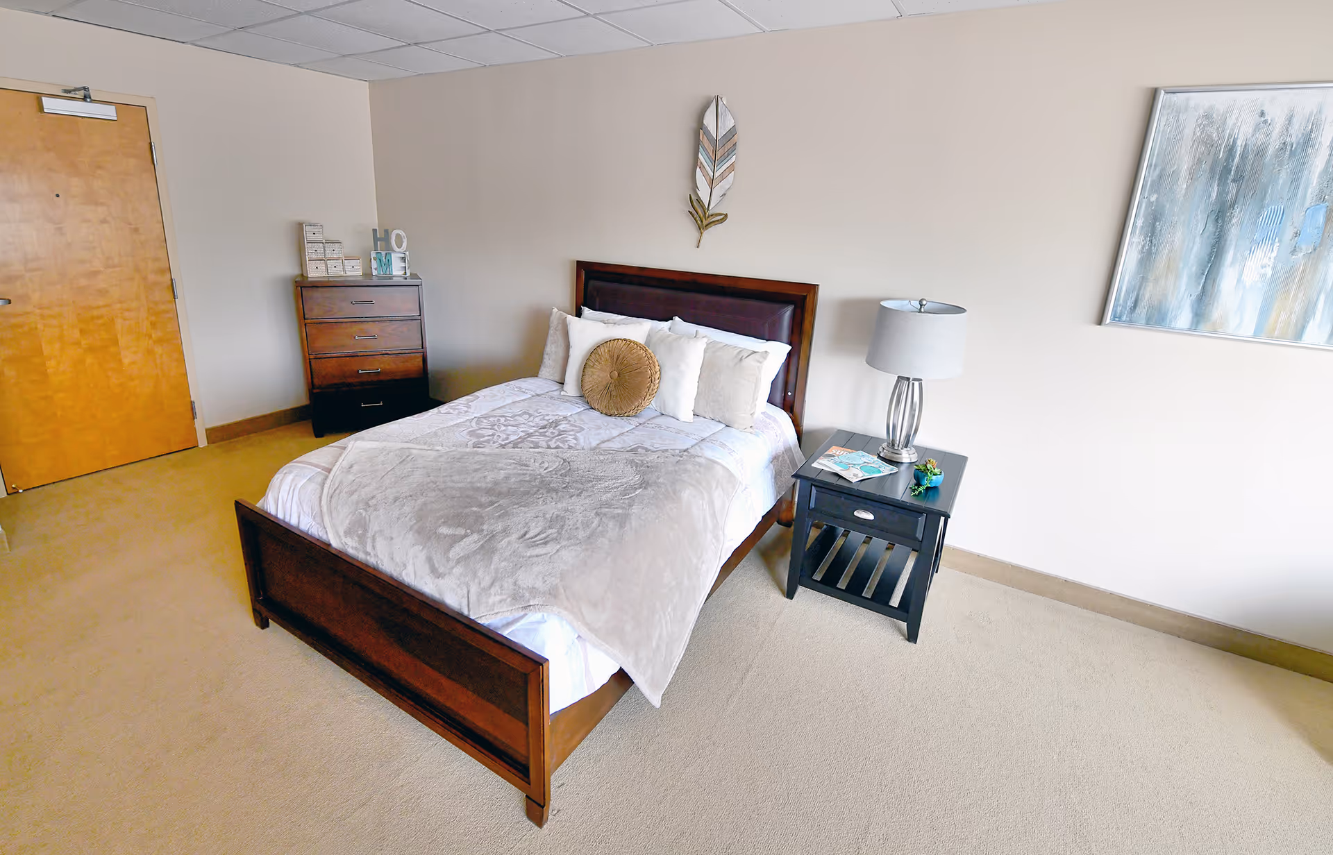A neatly made bedroom with a wooden bed, nightstand, dresser, and soft decor.