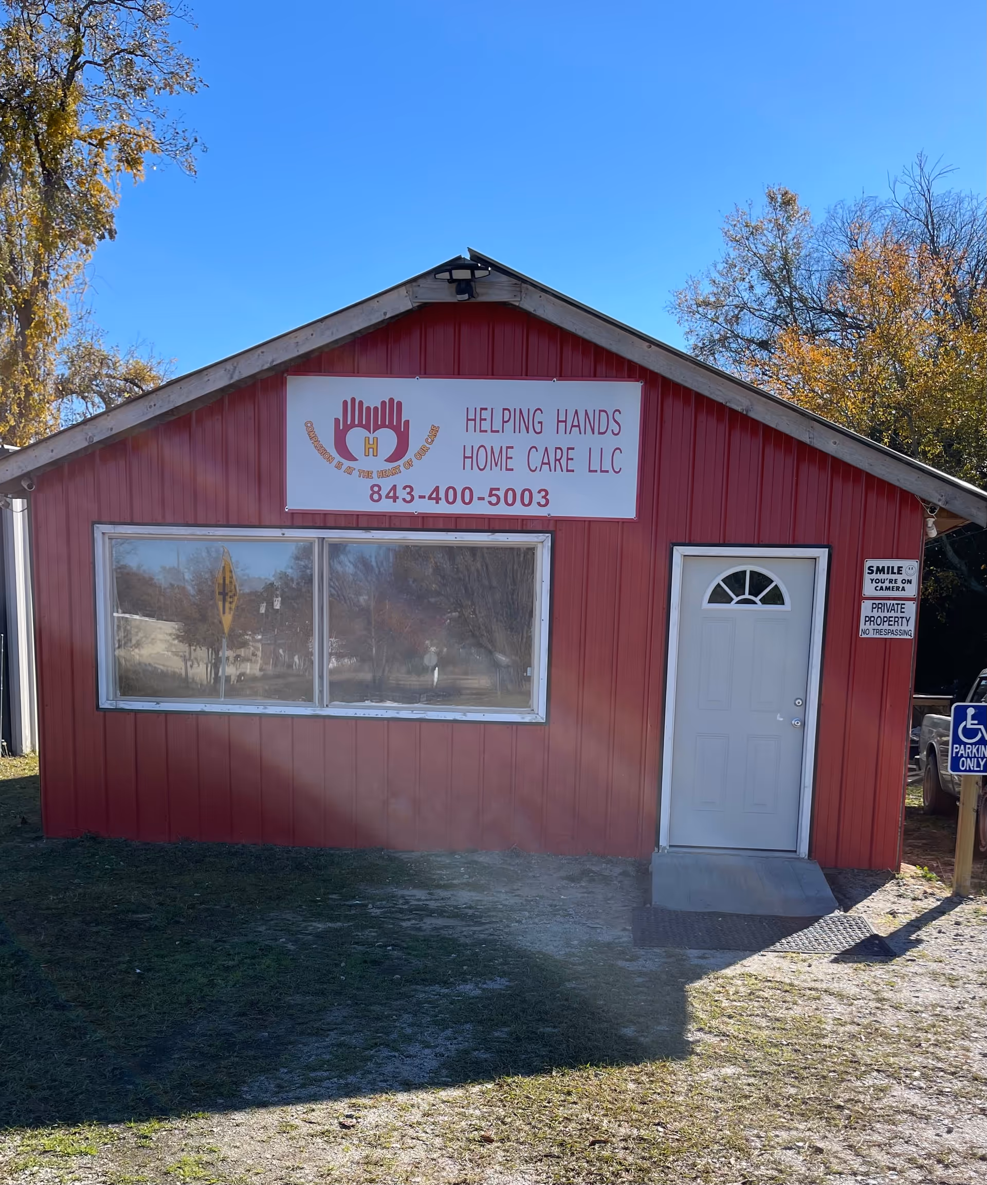 Front view of a red building with Helping Hands Home Care LLC sign and phone