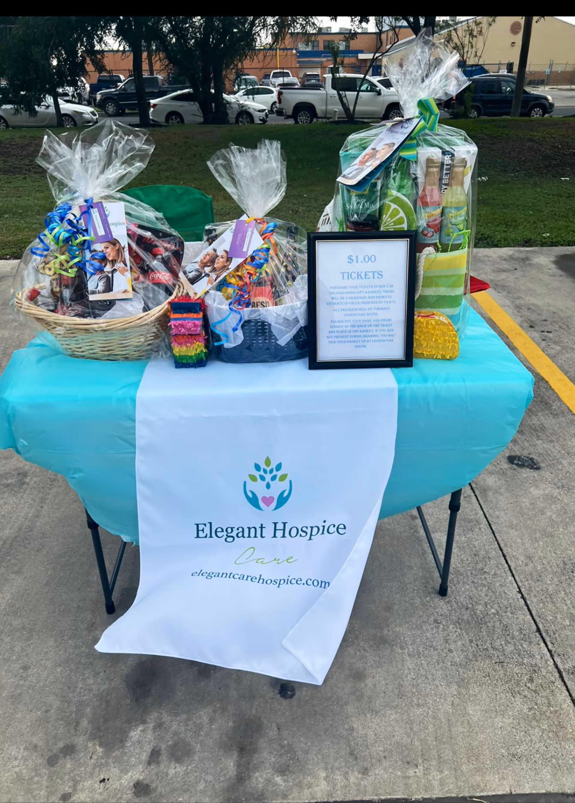 Outdoor table with teal tablecloth, gift baskets, and a framed ticket sign for Elegant Hospice Care.