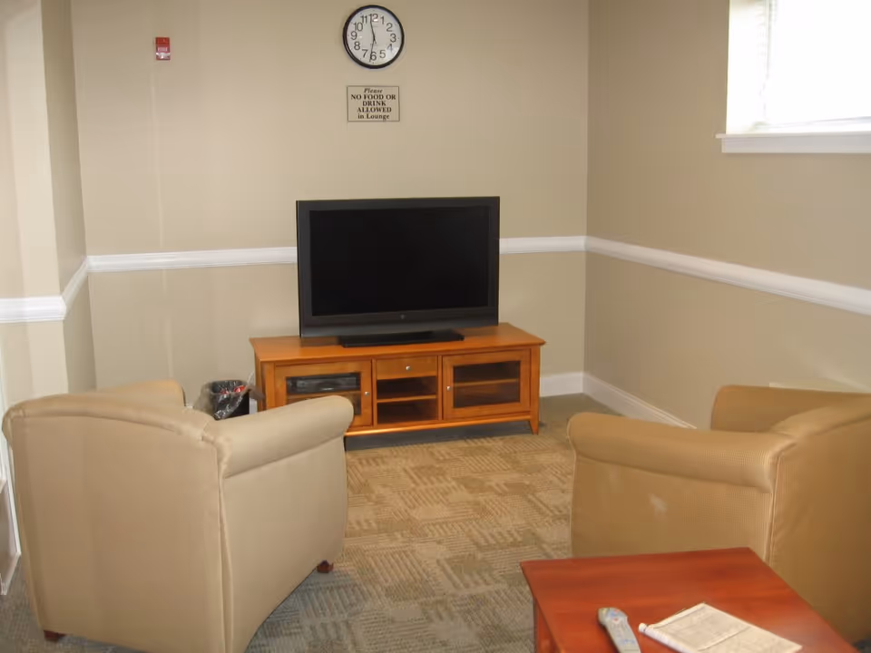 A small living room in a senior facility featuring beige chairs and a television.