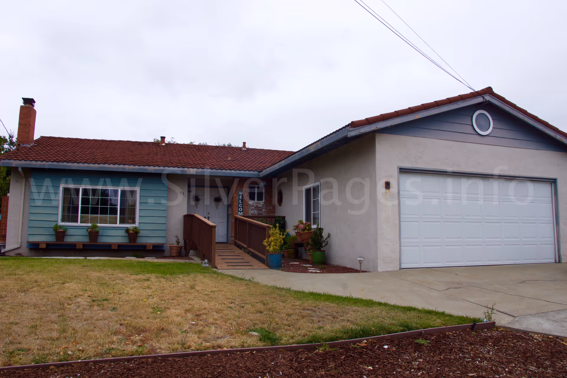Single-story care home exterior with a ramp, garage, and potted plants.