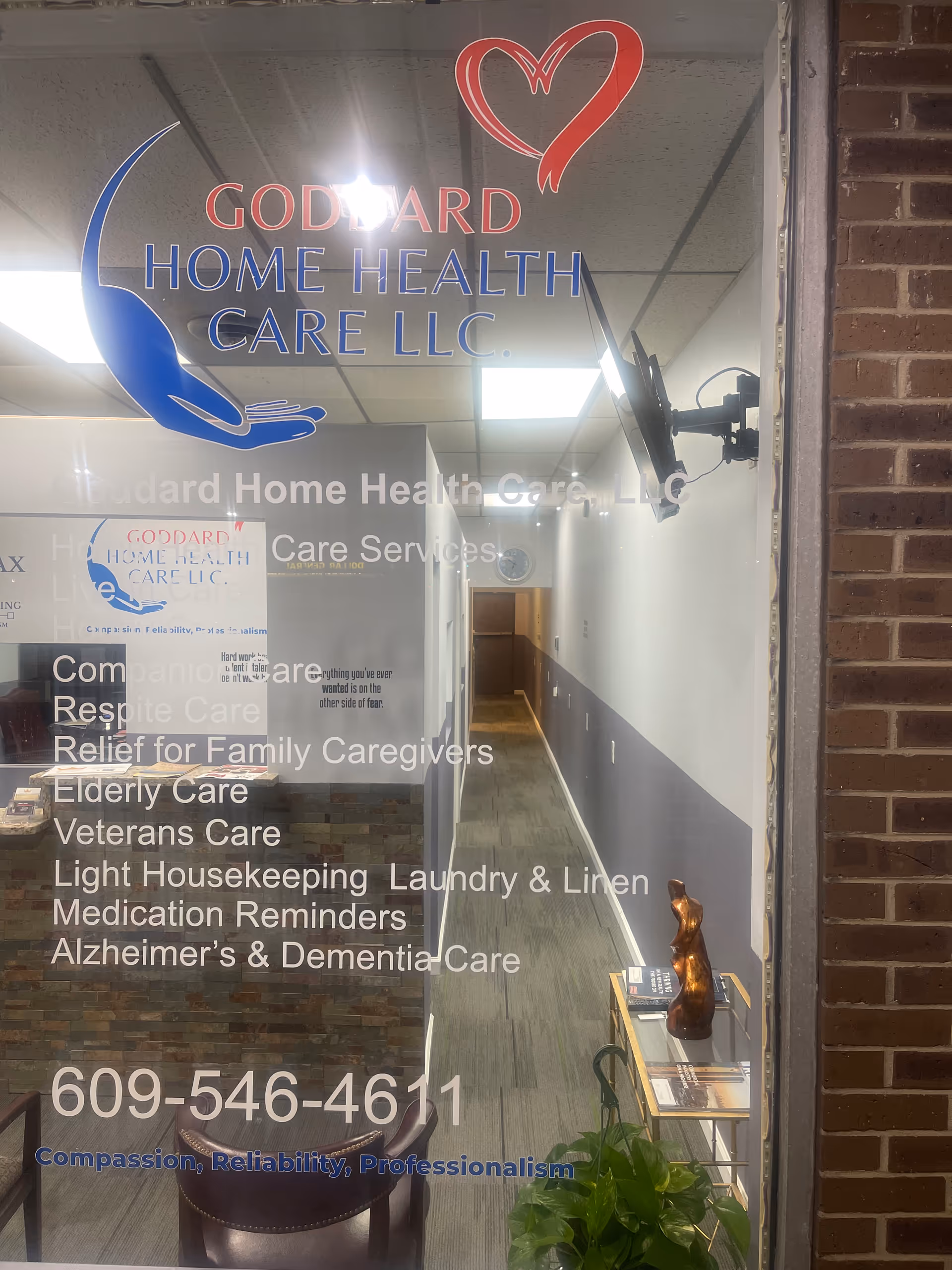 Glass storefront shows interior hallway of Goddard Home Health Care LLC, with signage and furniture.
