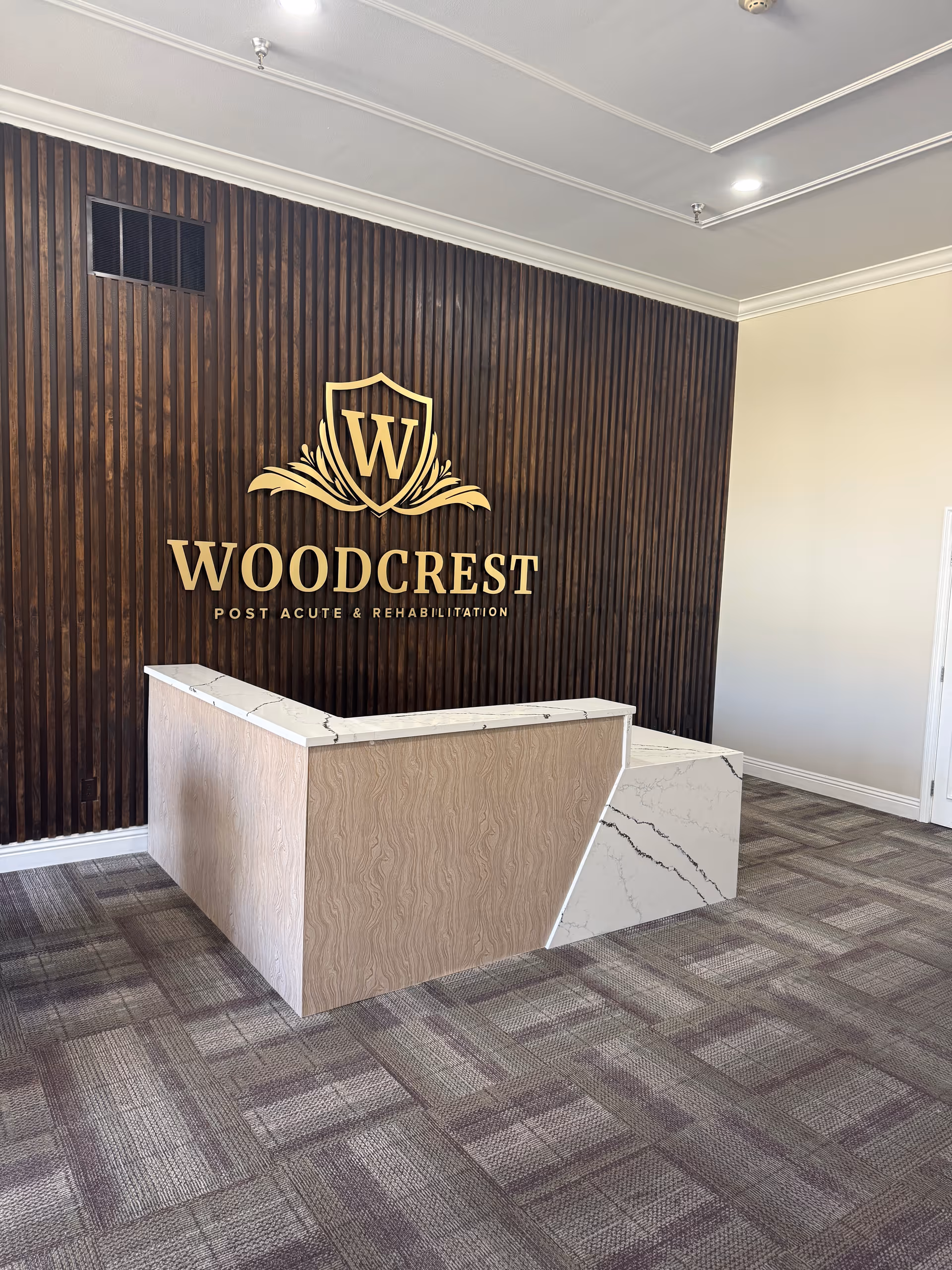 Woodcrest lobby reception desk against dark wood paneled wall with gold logo