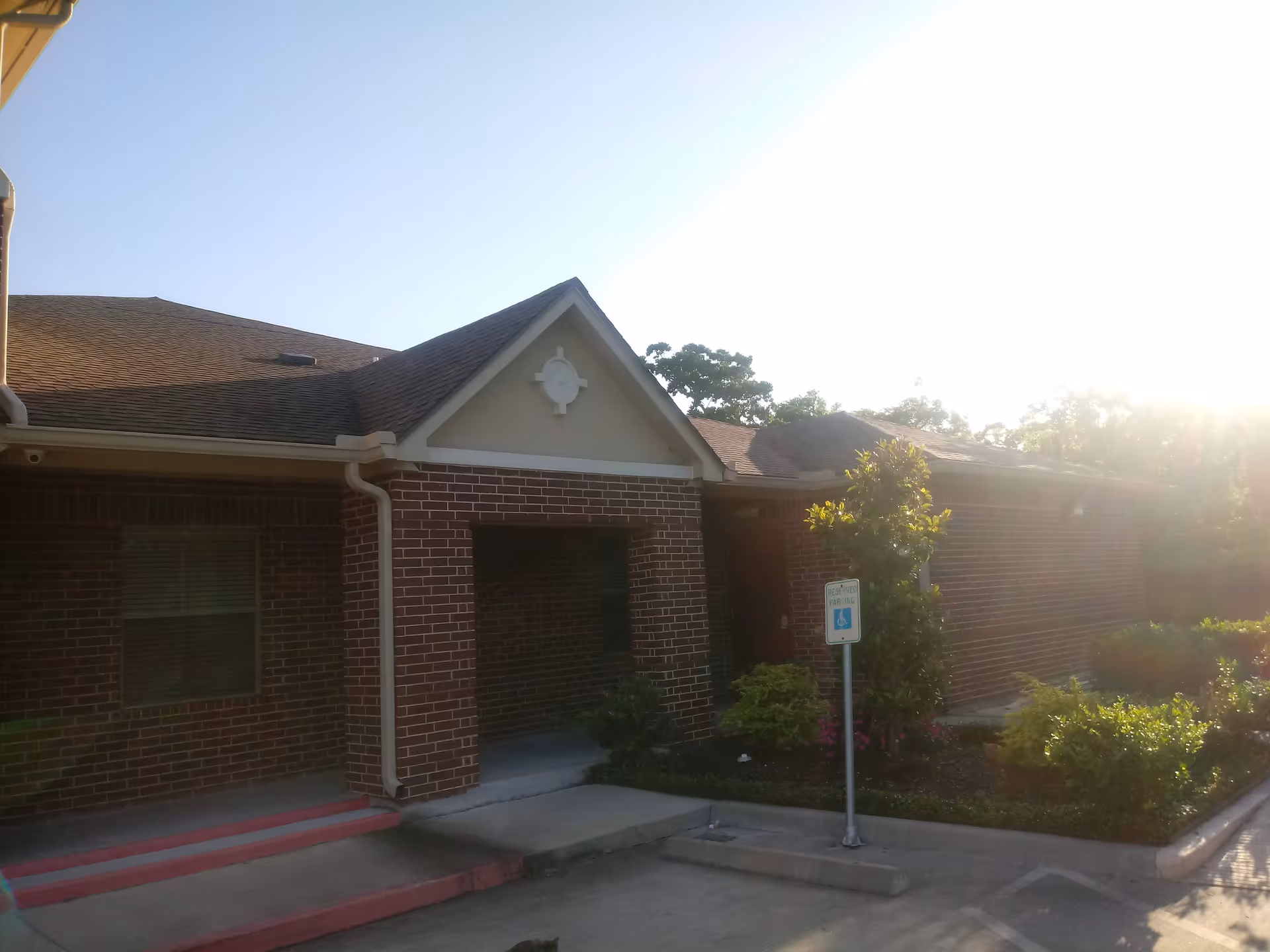 Brick exterior of a senior living facility with entrance, landscaping, and a handicap parking sign.