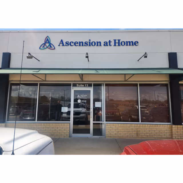 Front exterior of Ascension at Home facility with glass doors and sign.