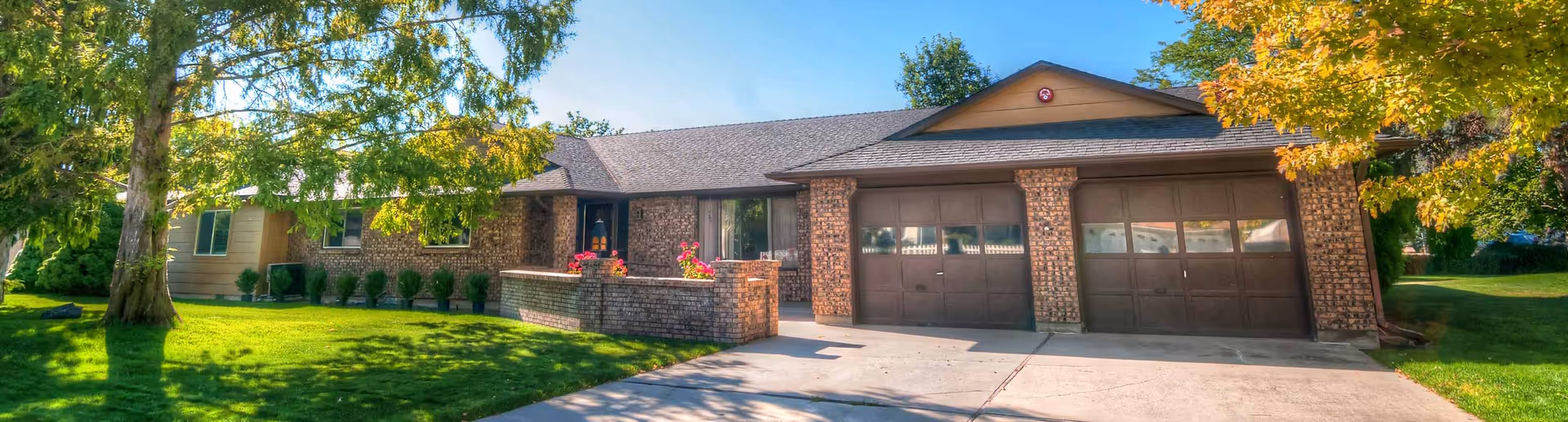 Single-story brick assisted living building with an attached two-car garage, front lawn, and trees.