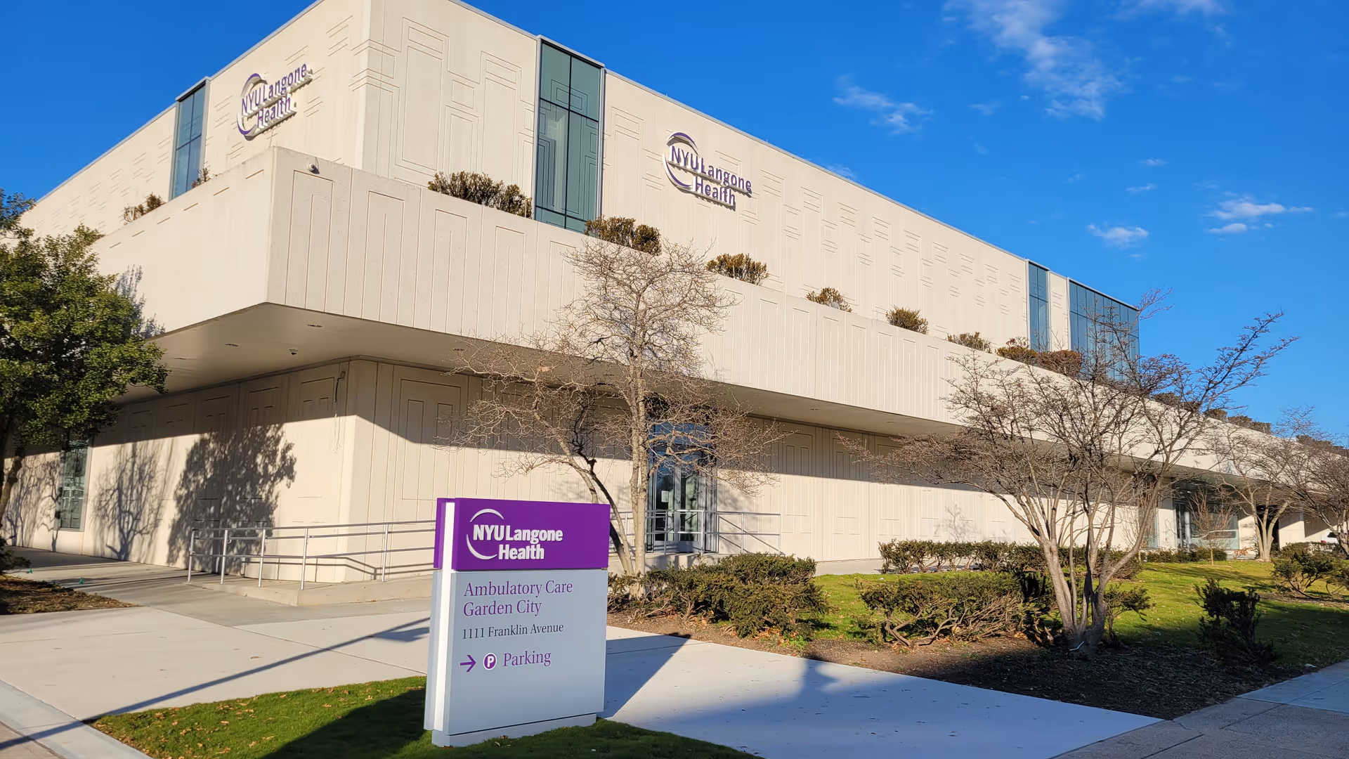 Modern beige medical building with NYU Langone Health signage and a purple information sign.