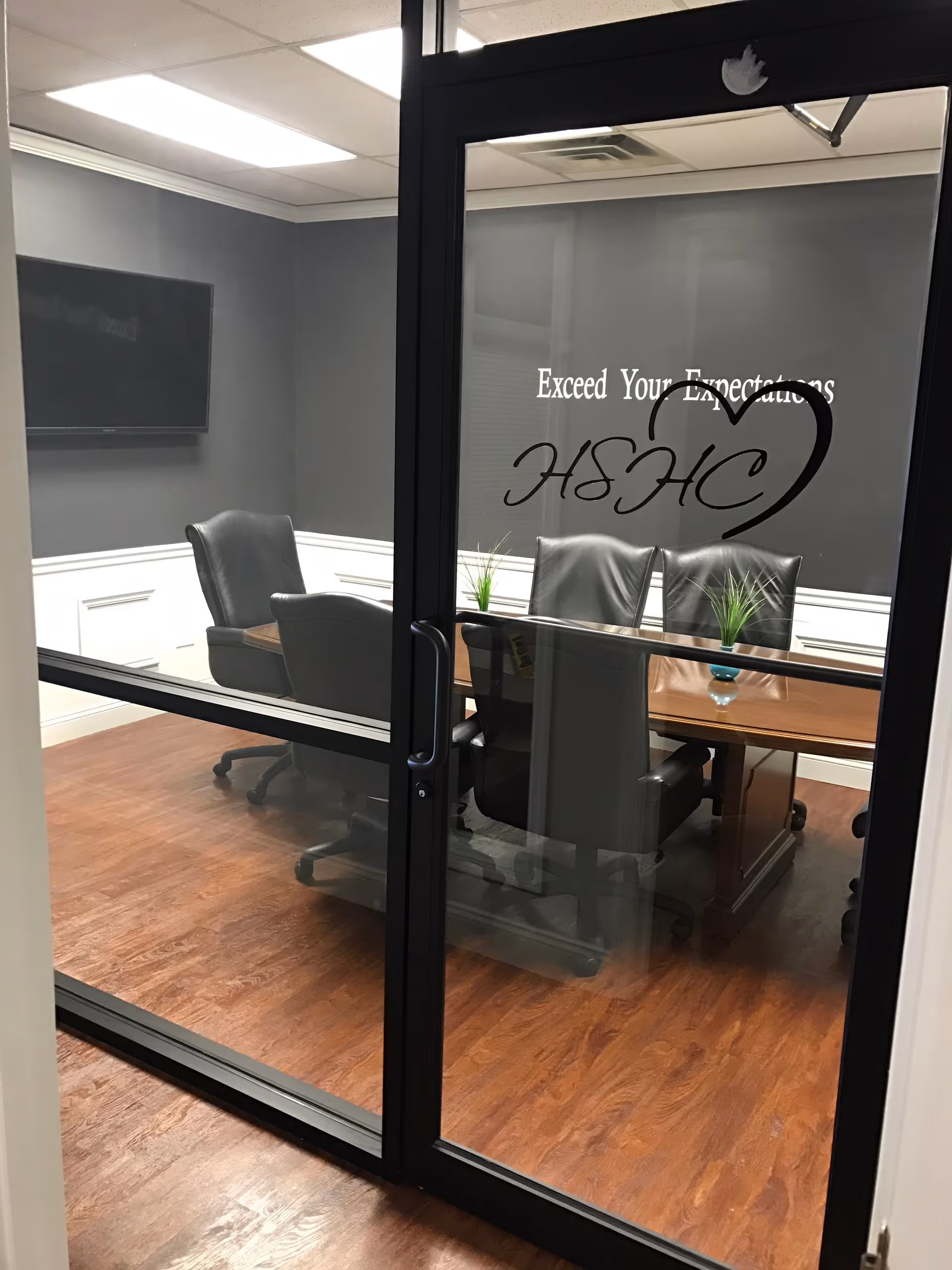 Glass-door conference room with wooden floor, black chairs, and a table in a meeting space.