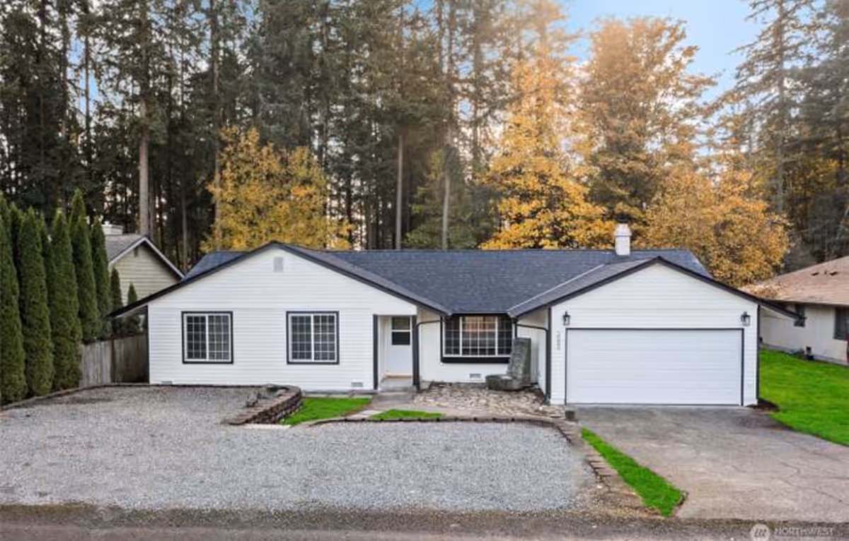White single-story house with attached garage and autumn trees behind it.