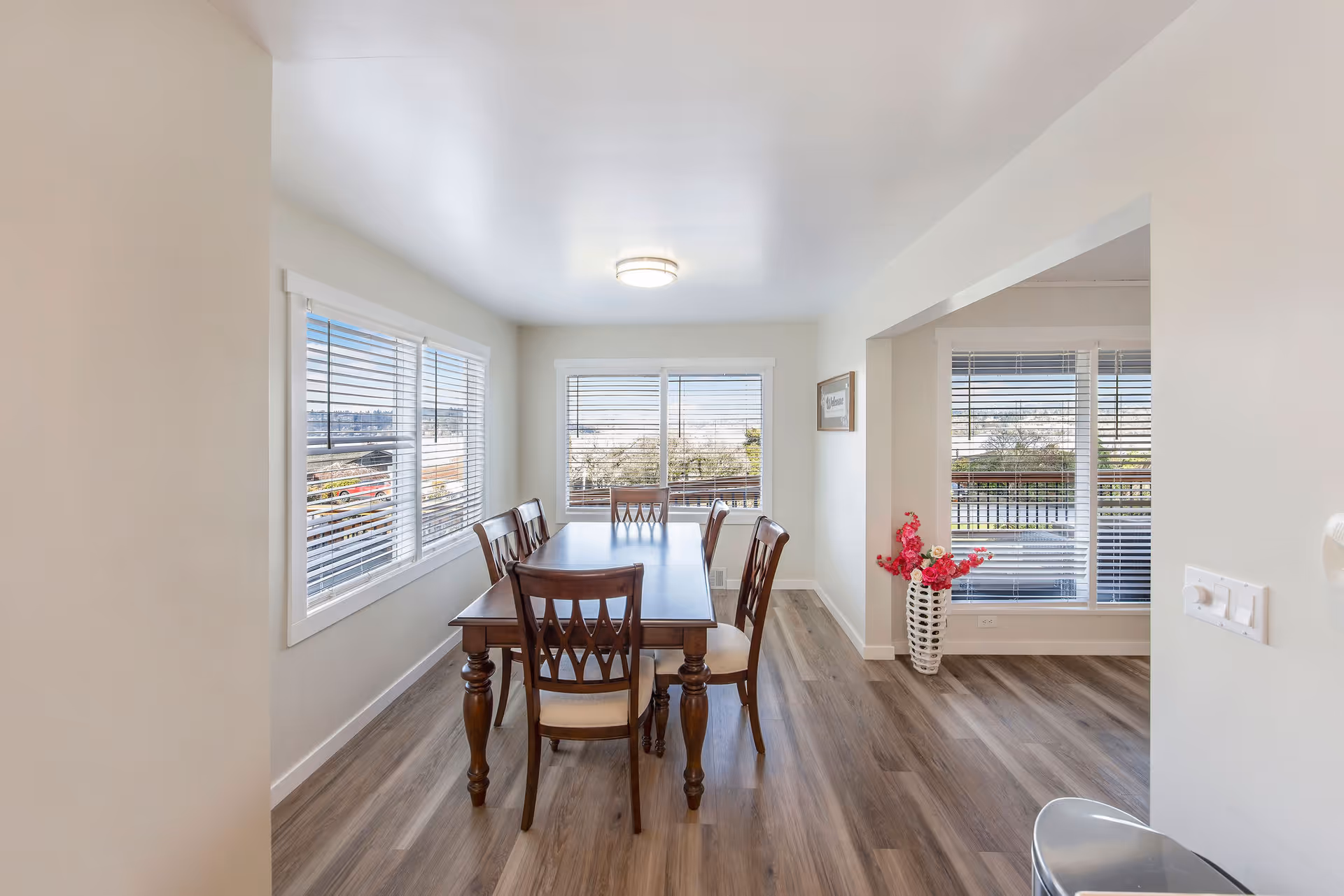 Bright dining room with a wooden table and chairs beside large windows.