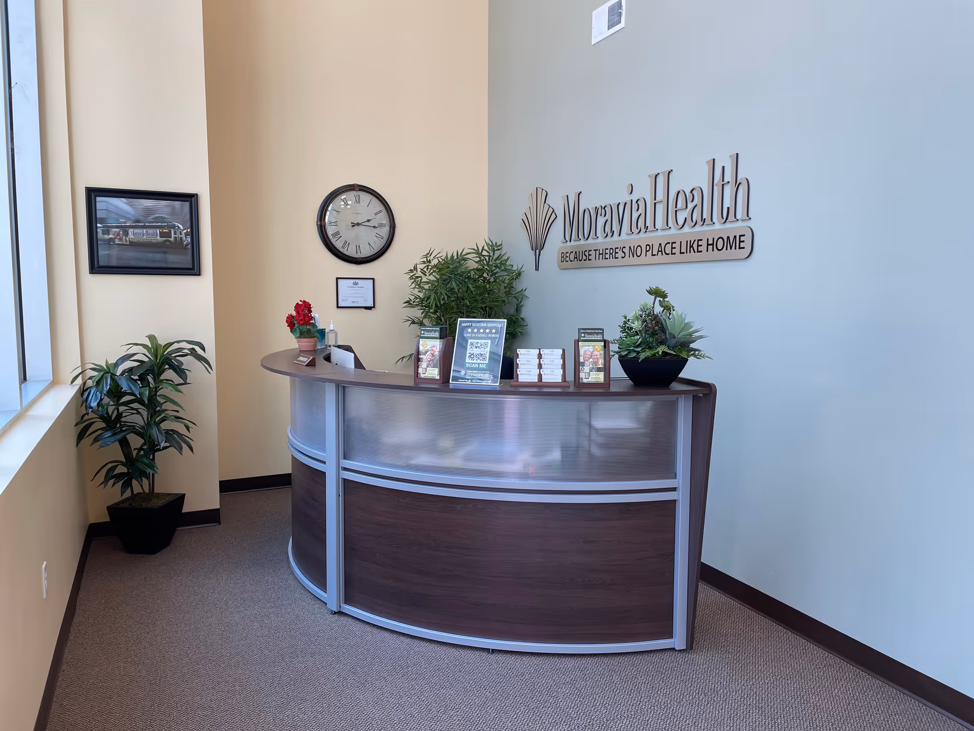 Reception desk in a modern lobby with Moravia Health sign, clock, and plants.