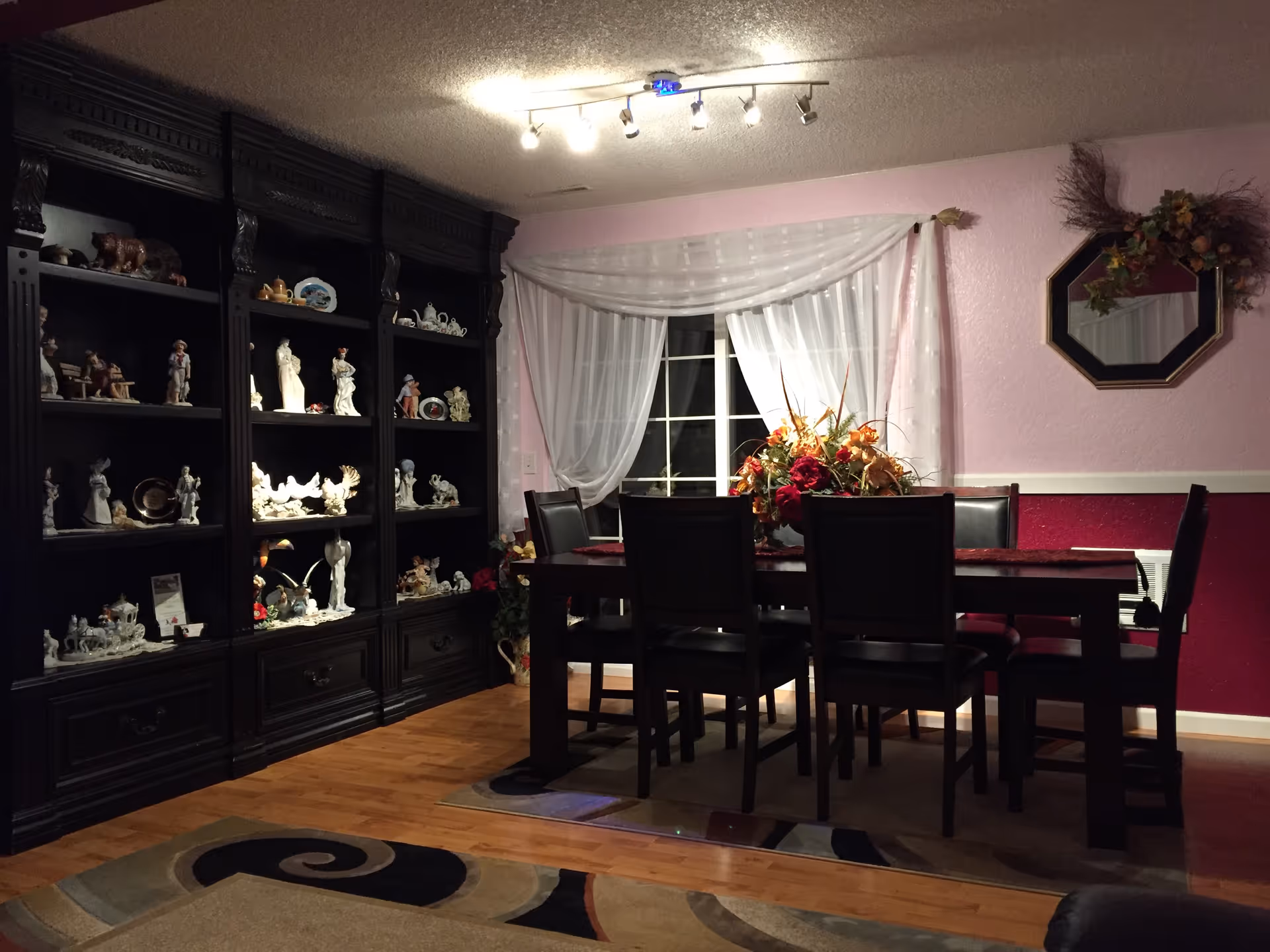Dark wood dining room with a long table, display cabinet, and floral centerpiece.
