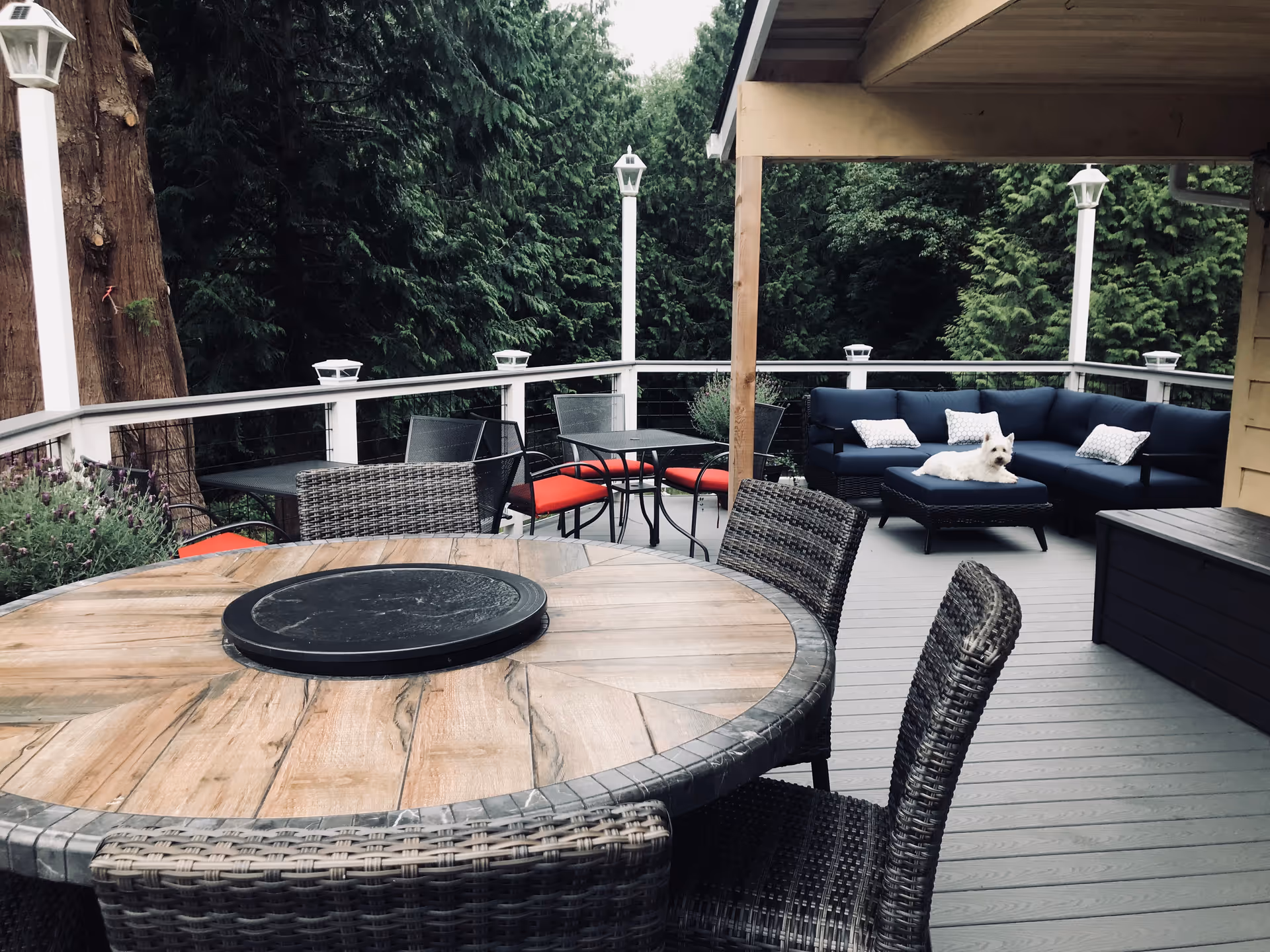 Spacious outdoor deck with wicker chairs, a round table, blue sectional couch, and a white dog.
