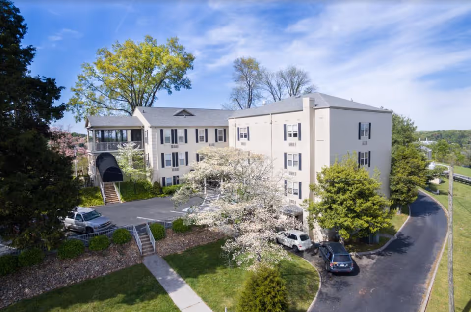 River Oaks Place Loudon: beige multi-story senior living building with curved driveway and trees.