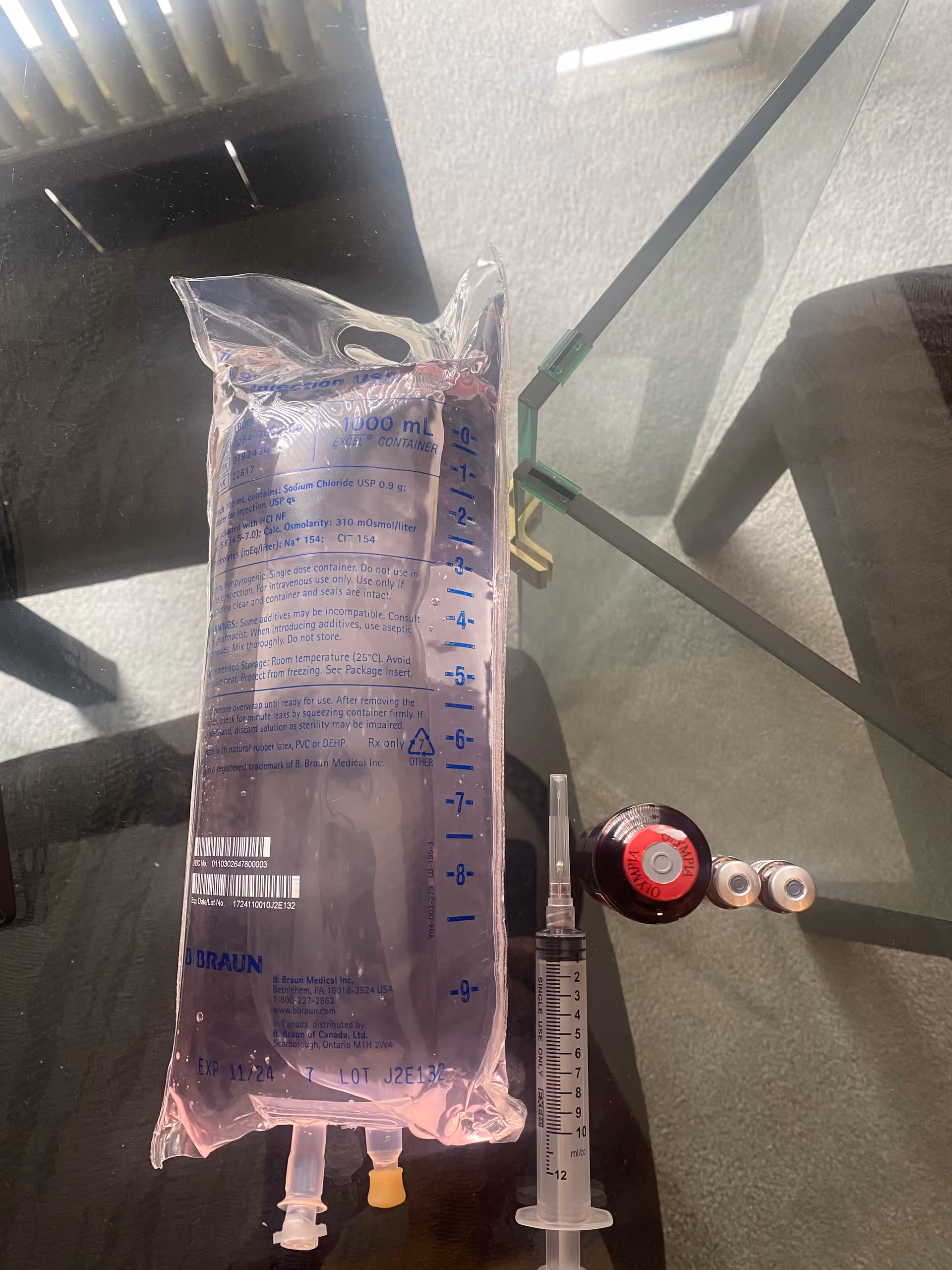 IV bag, syringe, and tubing on a glass table in a medical setup.