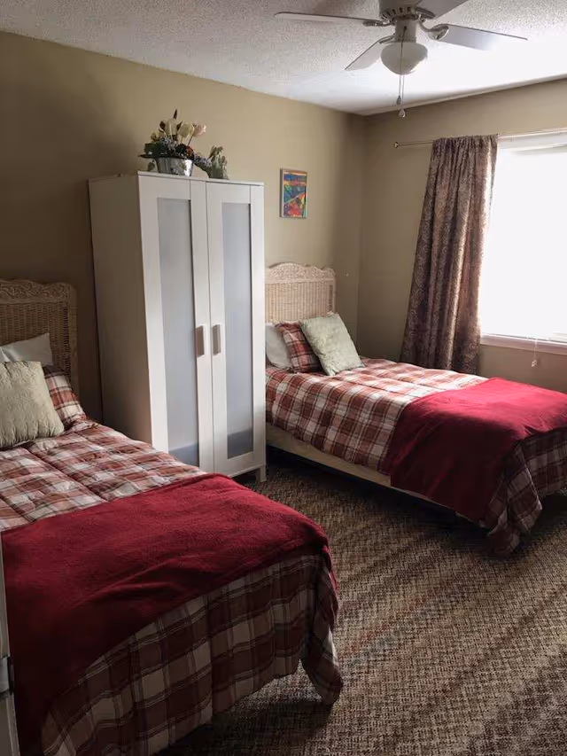 Two single beds with plaid bedding and a white wardrobe in a beige bedroom.