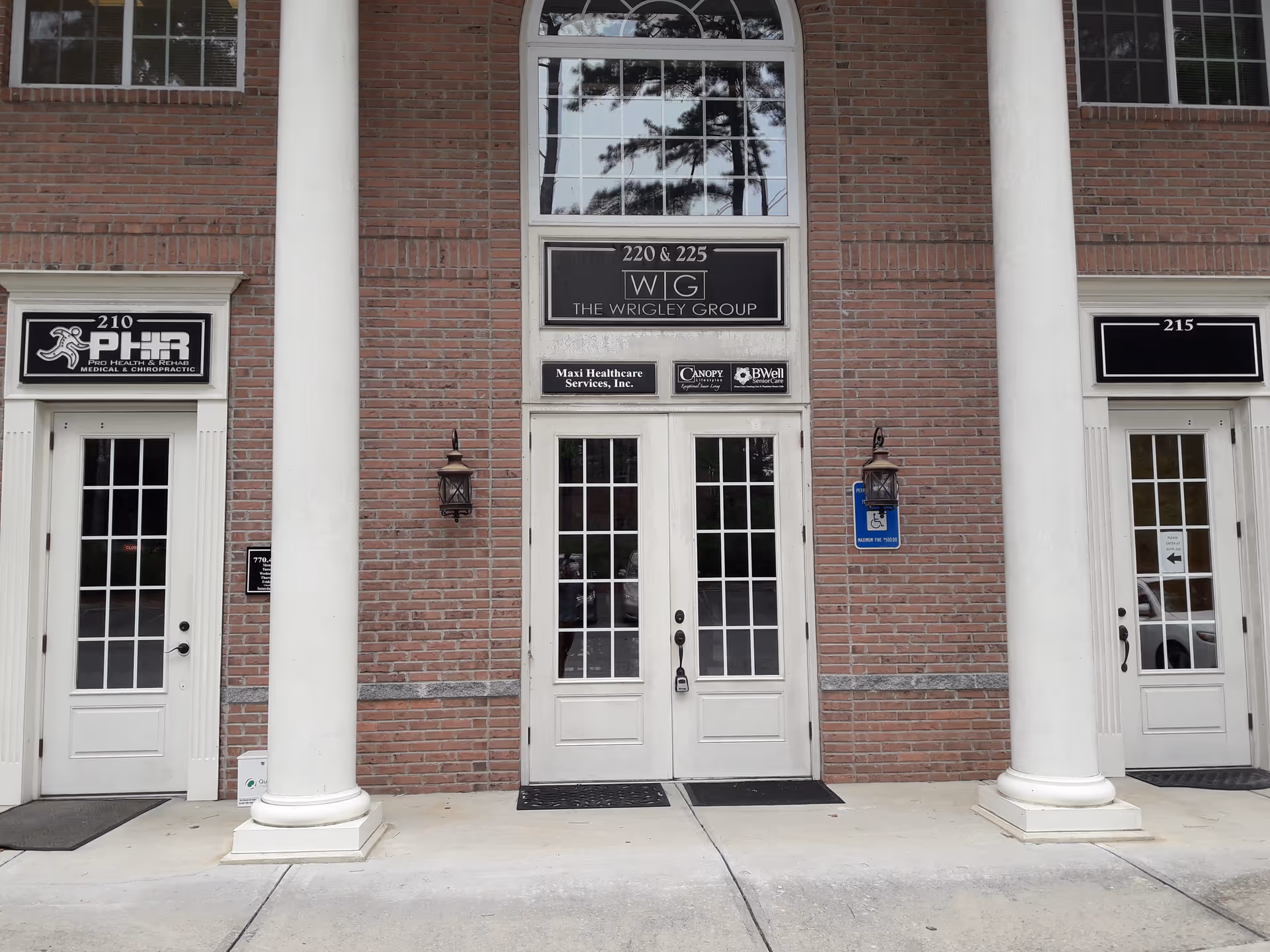 Brick building front with white columns, glass doors, and signs including Maxi Healthcare.