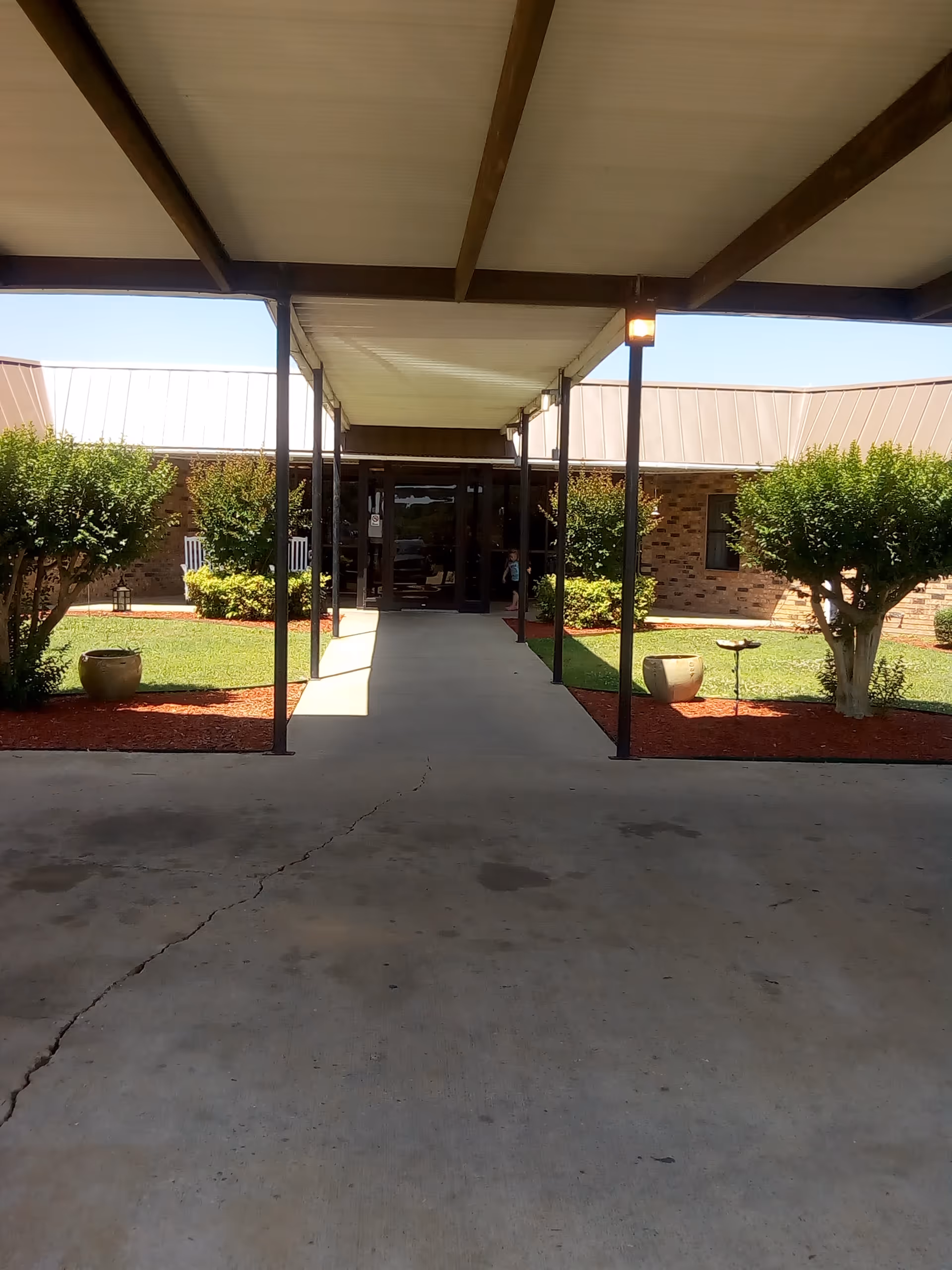 Covered walkway to brick building entrance with shrubbery and lighting
