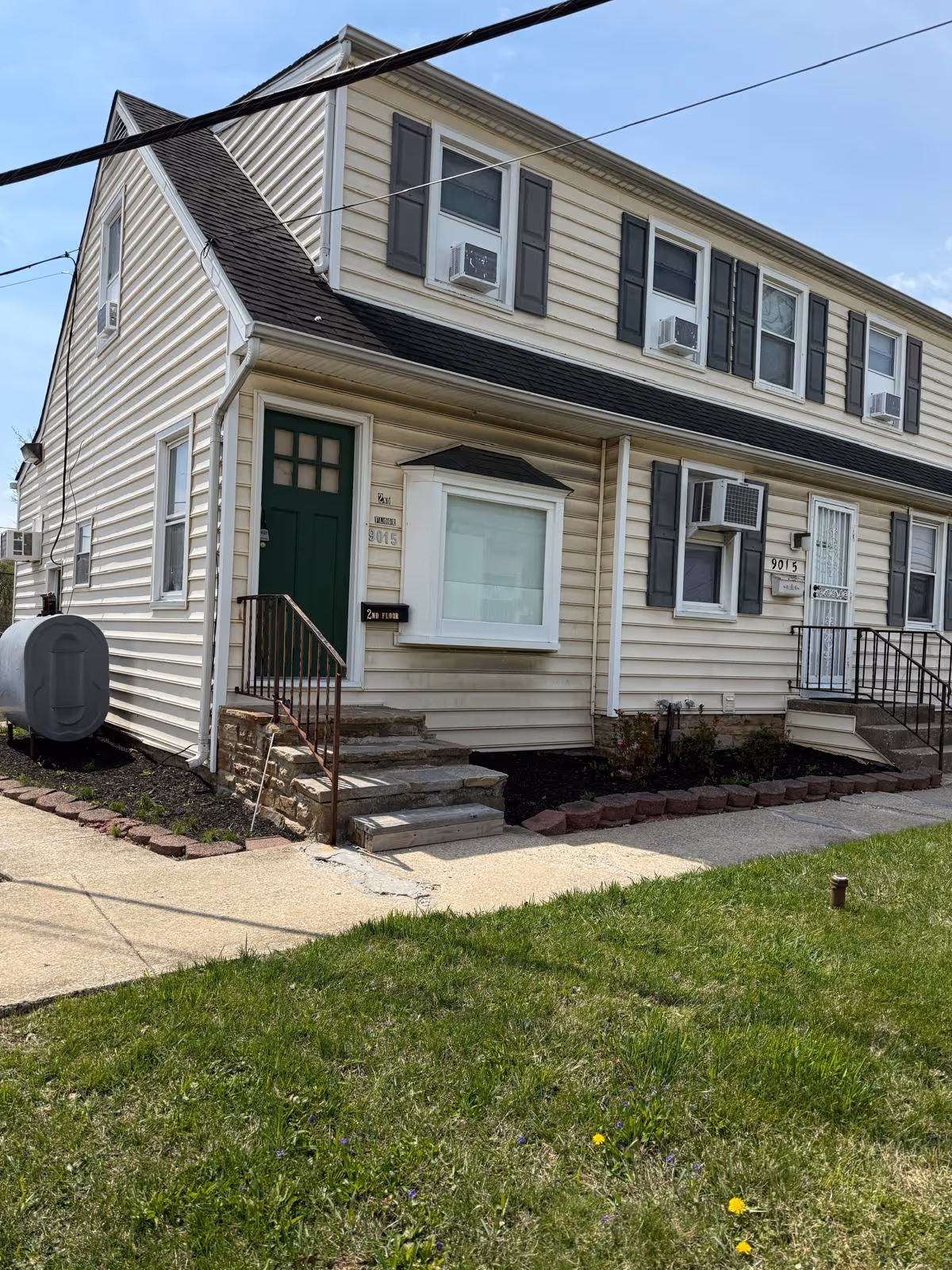 Two-story beige senior living facility with green front door, stairs, and surrounding lawn.