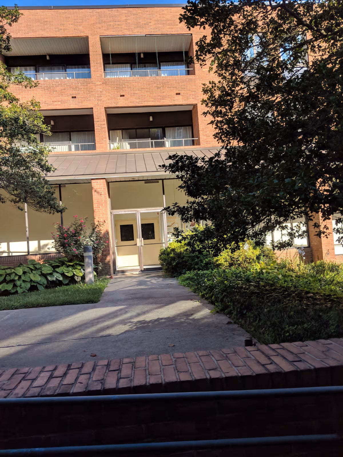 Stella Maris building entrance with glass doors, brick facade, and surrounding greenery.