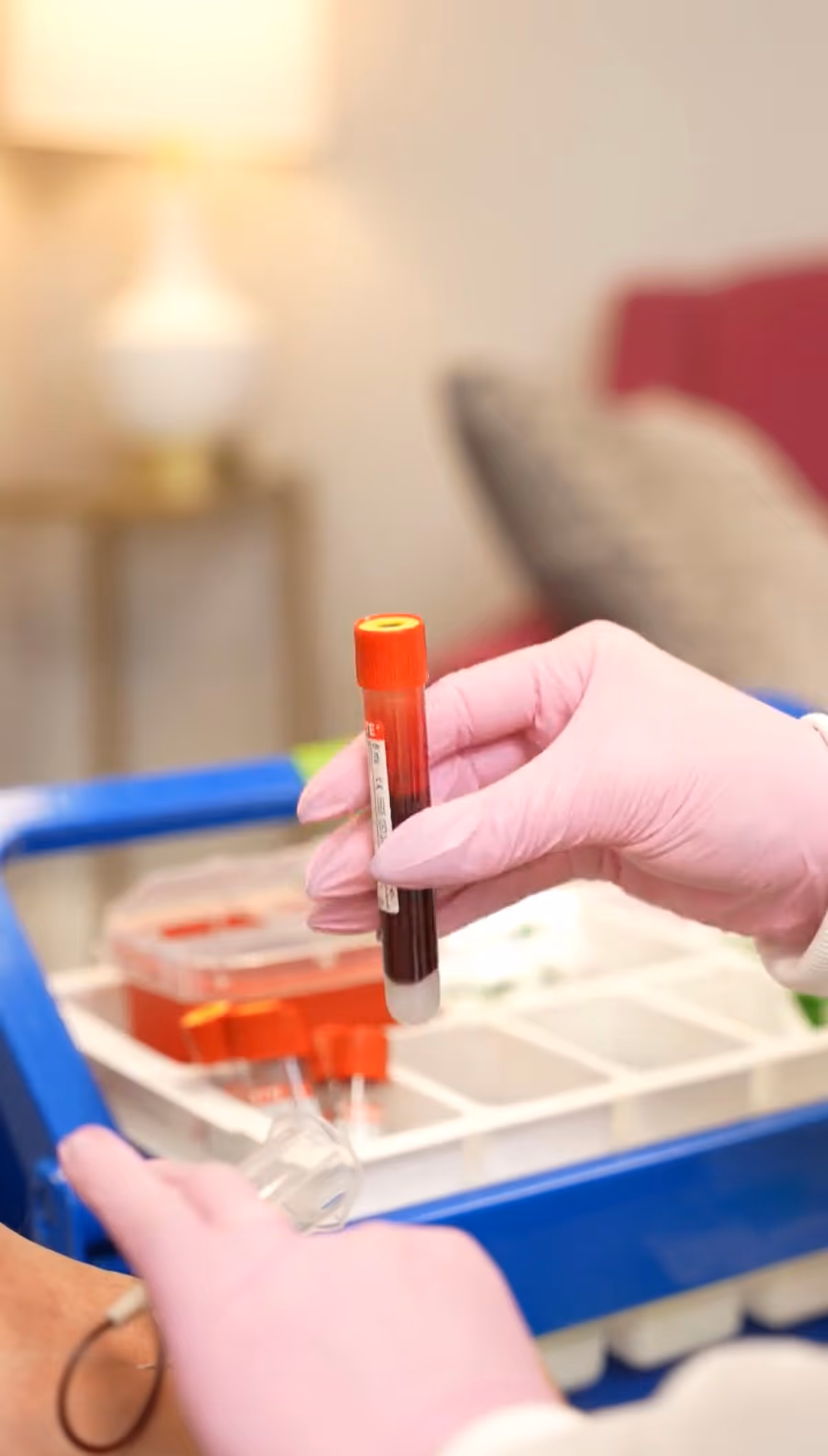 Gloved hands hold a blood sample tube beside a medical cart.