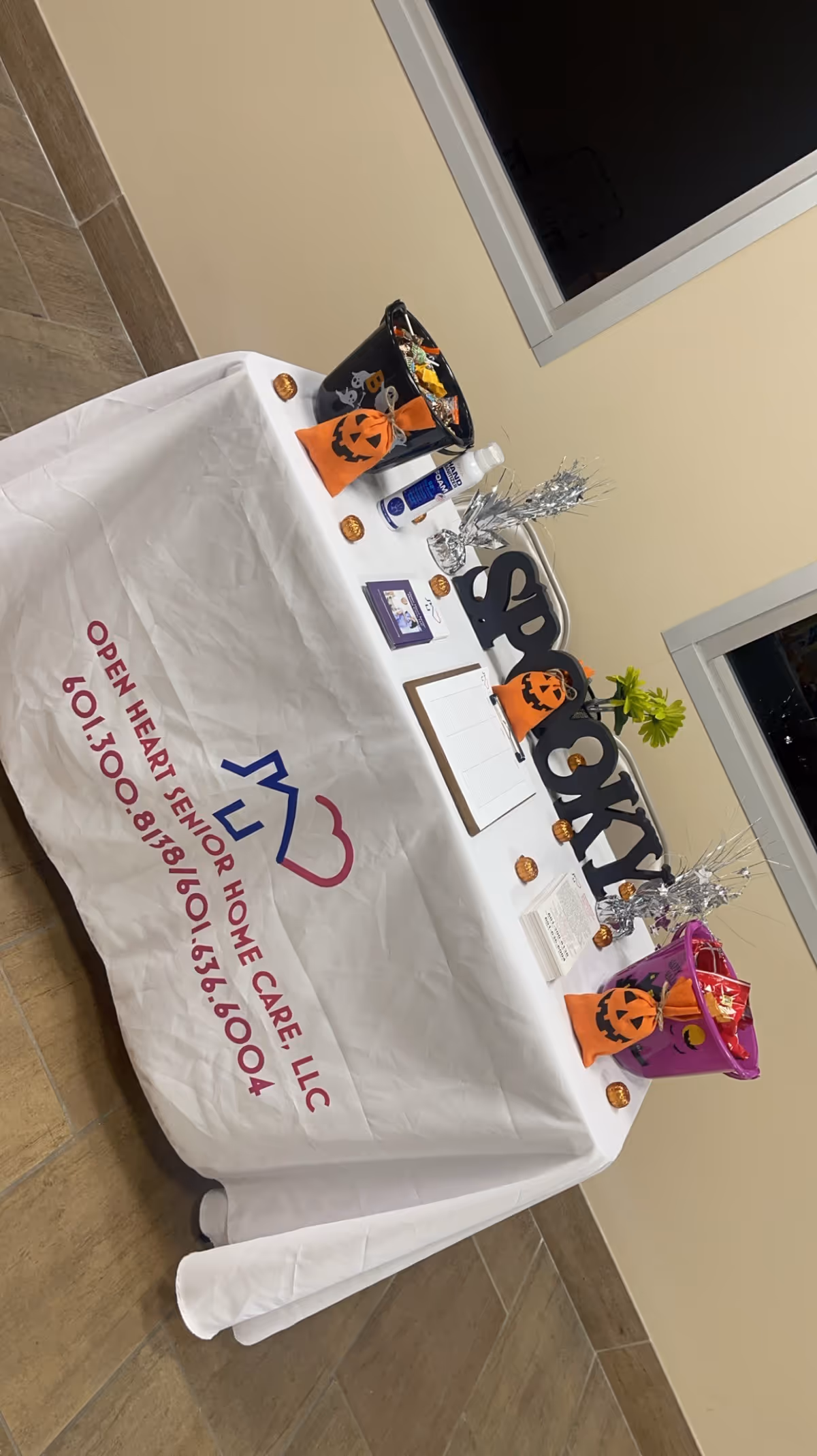 Promotional table with Open Heart Senior Care LLC logo and Halloween decor inside facility.