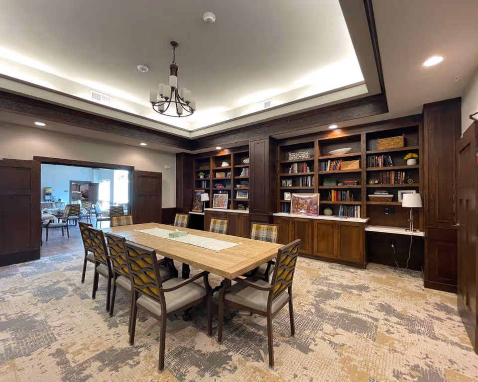 Interior dining room at Edencrest at Adel featuring a long wooden table and bookshelves.