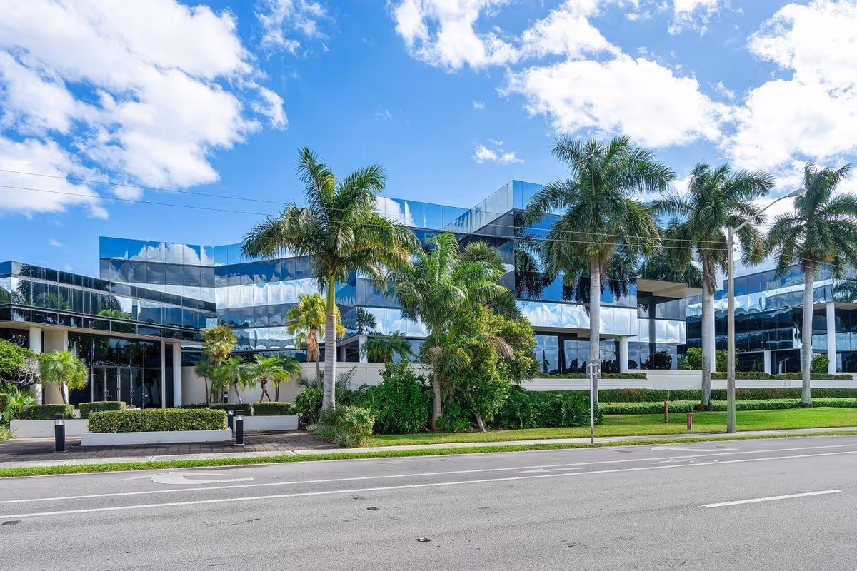 Modern glass-front senior living building with palm trees along a street.