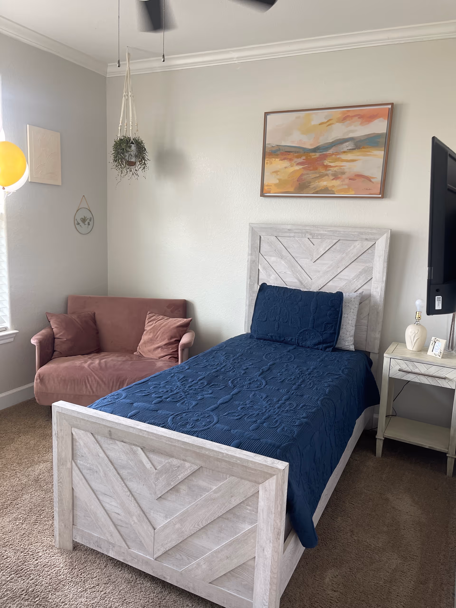 Bedroom with a whitewashed wooden bed, blue quilt, pink loveseat, and wall art.