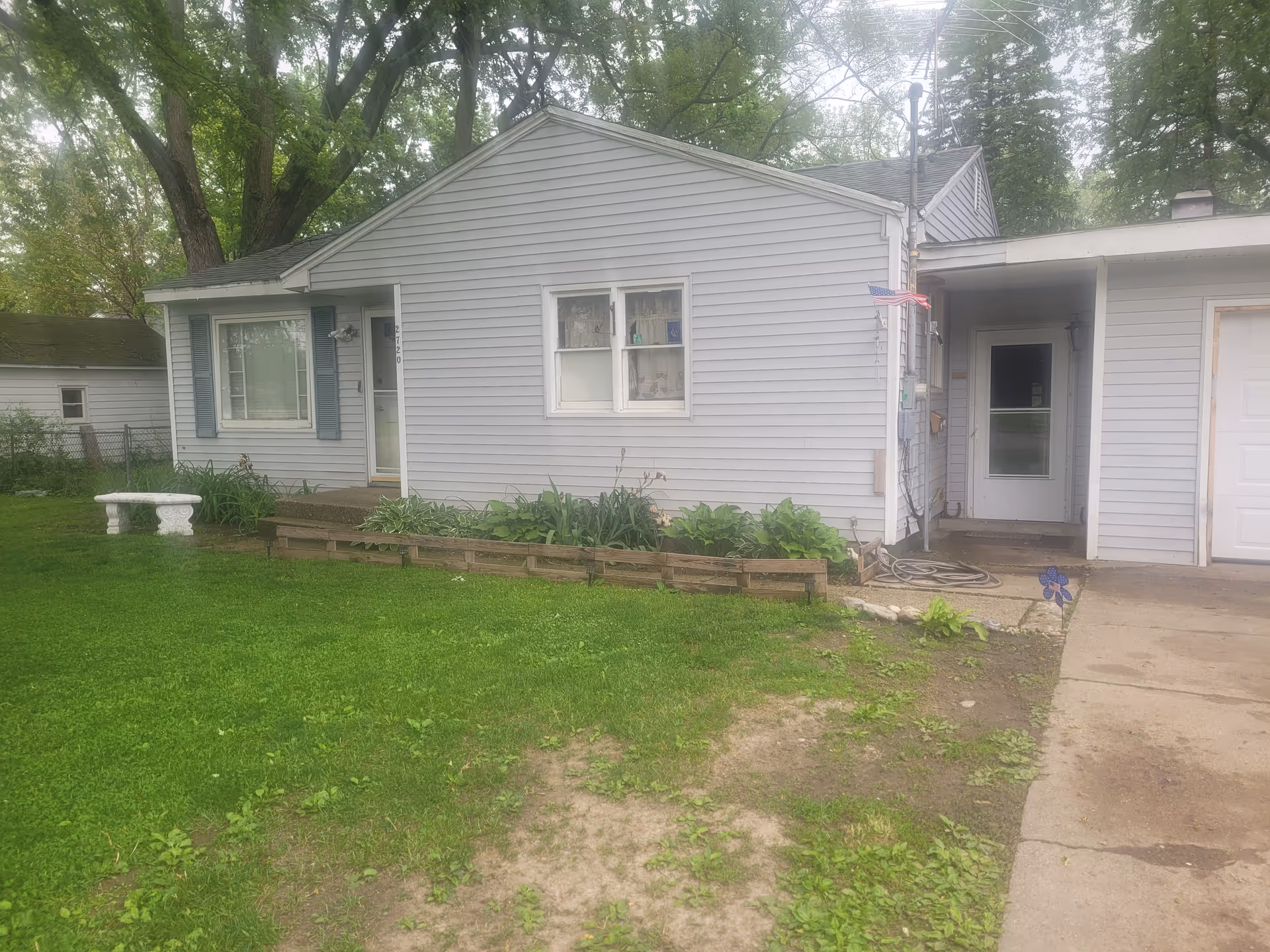 Gray, single-story house with a front garden bed, lawn, bench, and entry door.