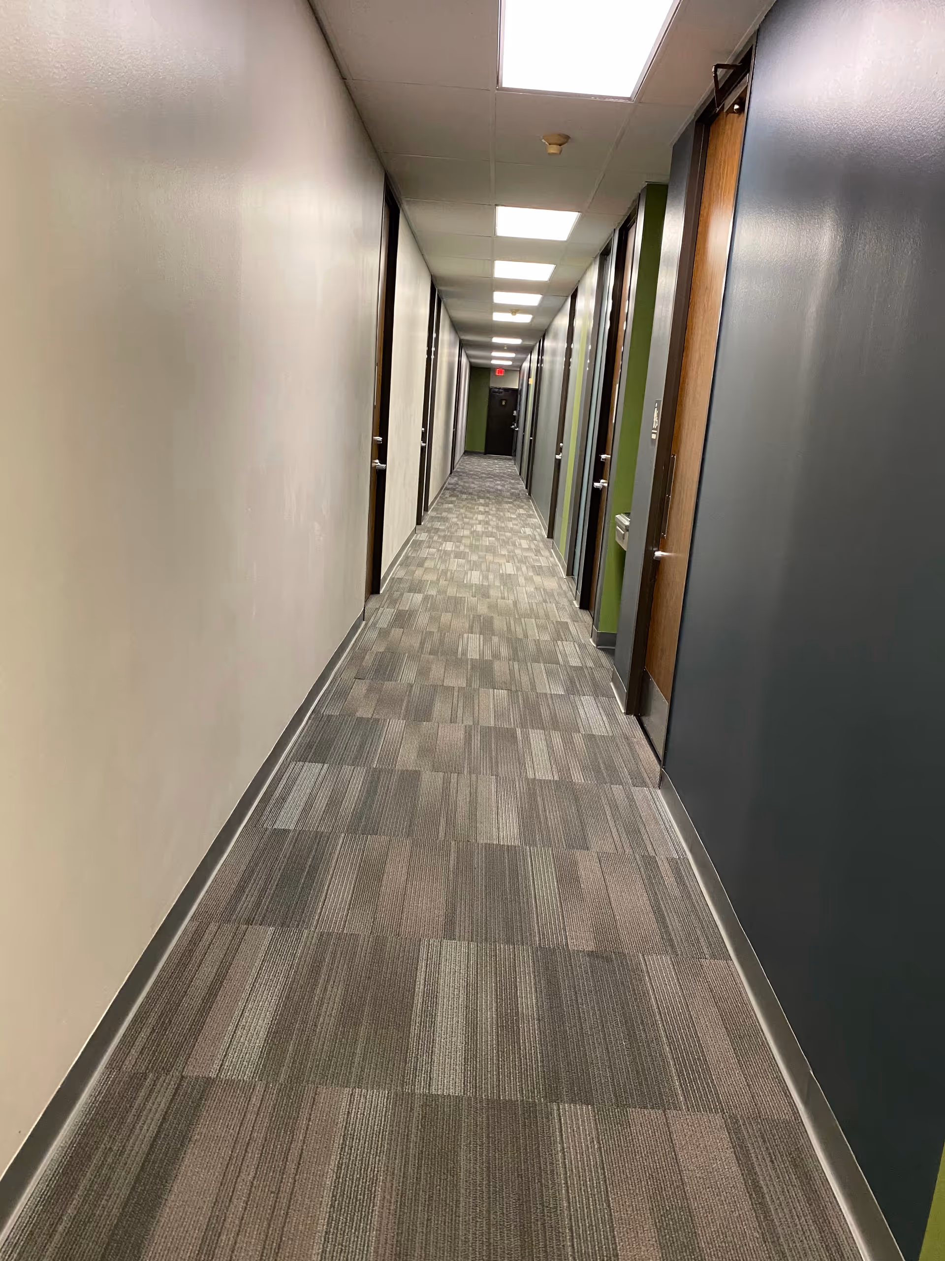 Bright, long corridor with closed doors and patterned carpet in a senior living facility.