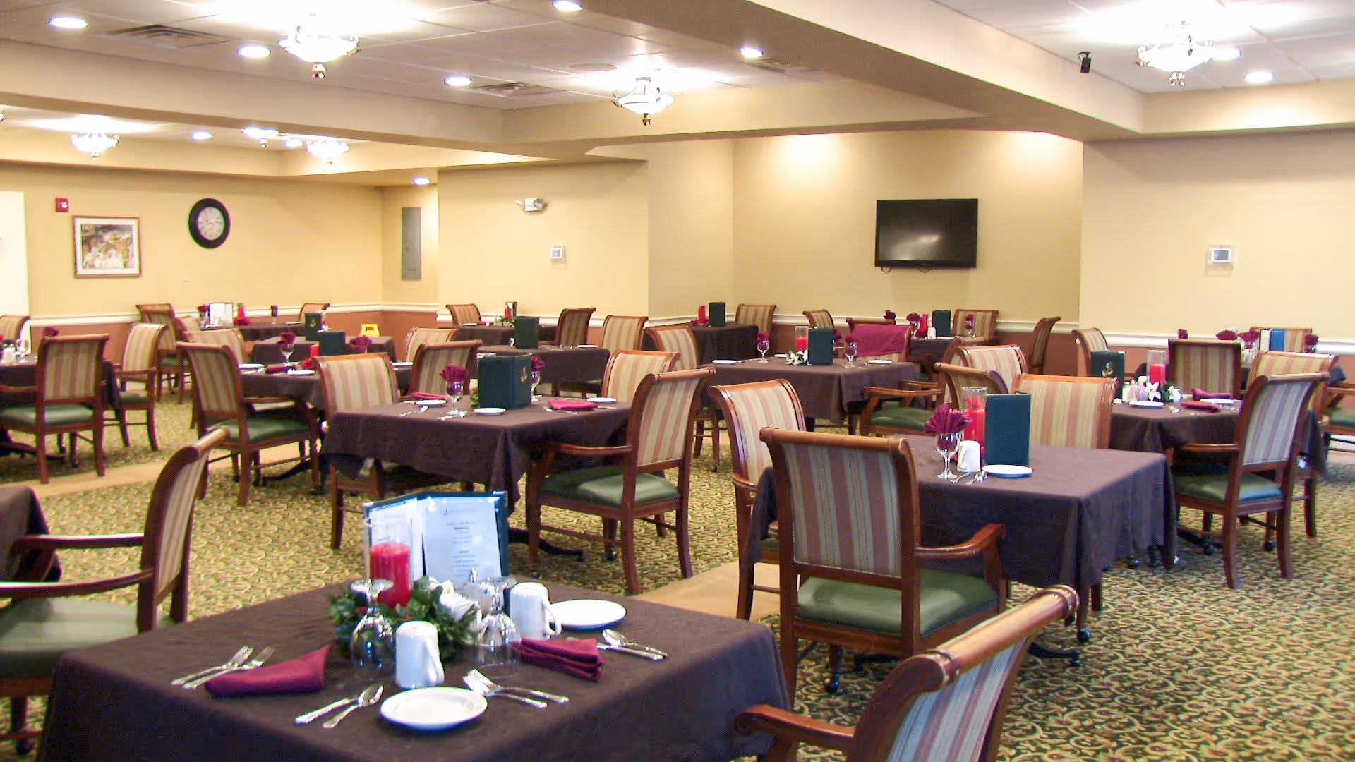 Spacious dining room in a senior facility with multiple tables set for meals.