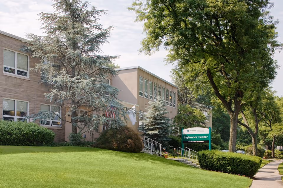 Exterior view of Inglemoor Center with green lawn, mature trees, and a sign.