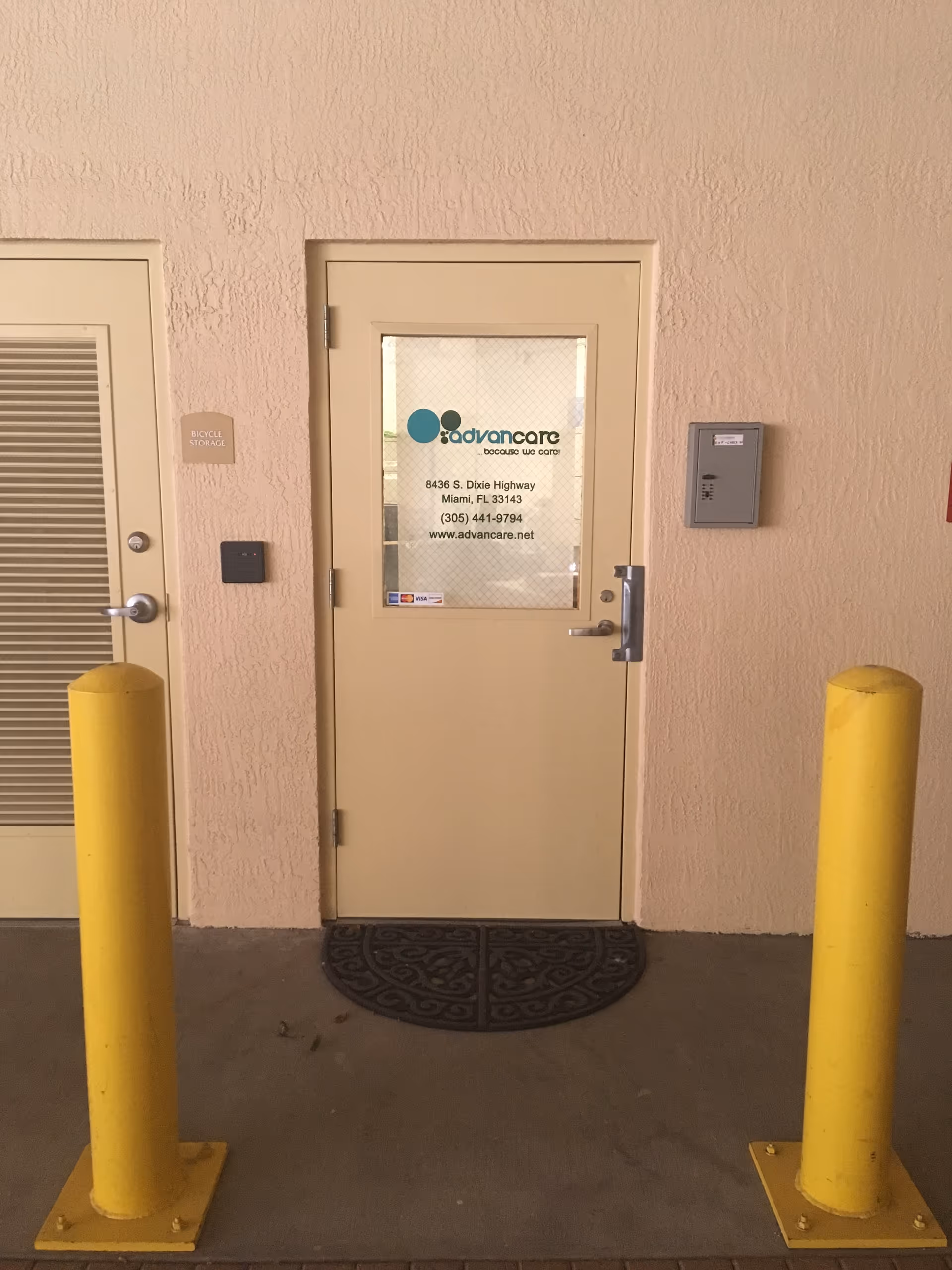 Interior hallway door labeled Advancare with two yellow bollards and a textured mat