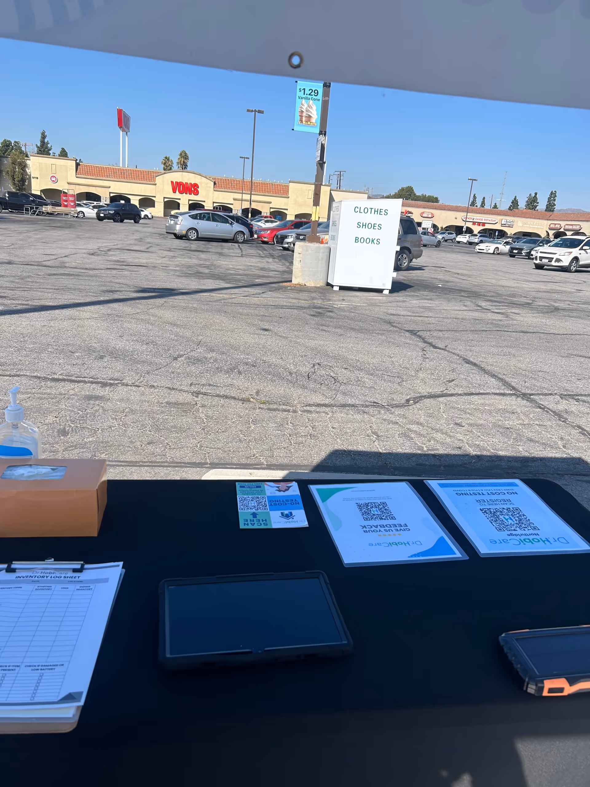 Outdoor check-in table in a parking lot with QR codes and informational papers.
