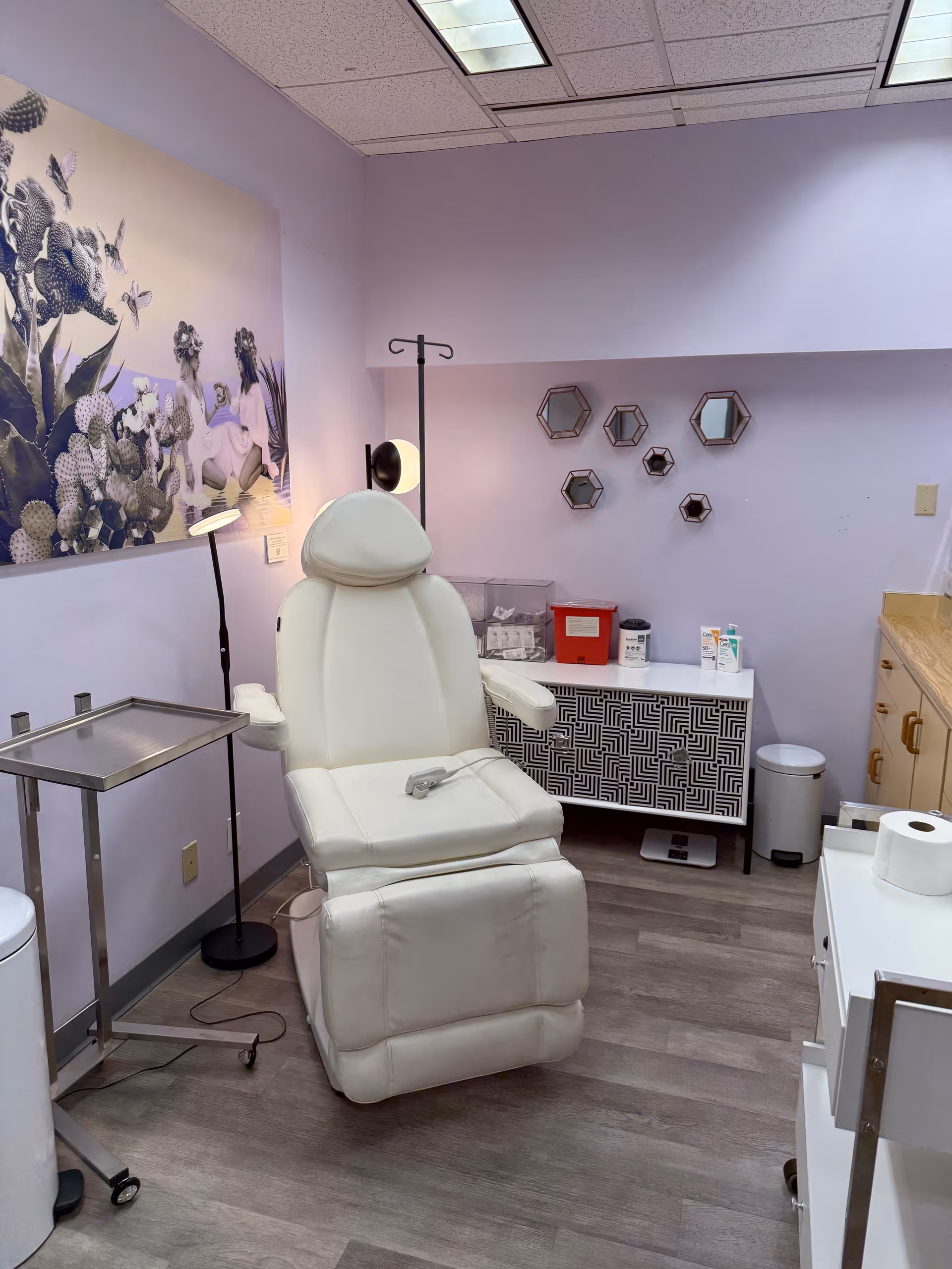 White medical recliner chair in a pastel purple treatment room with floral wall art.